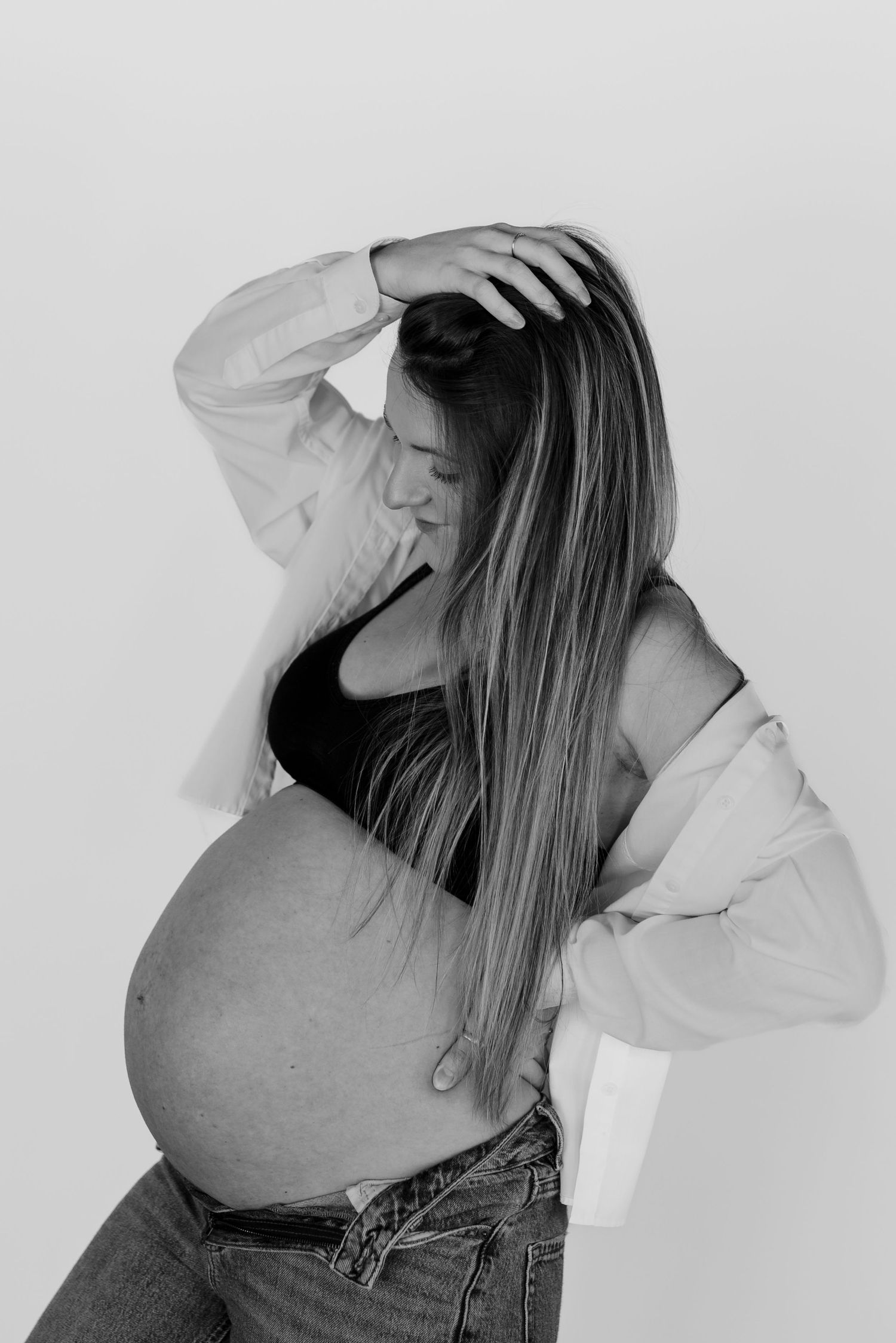 Black and white portrait of an expectant mother in casual attire posing against a light background.