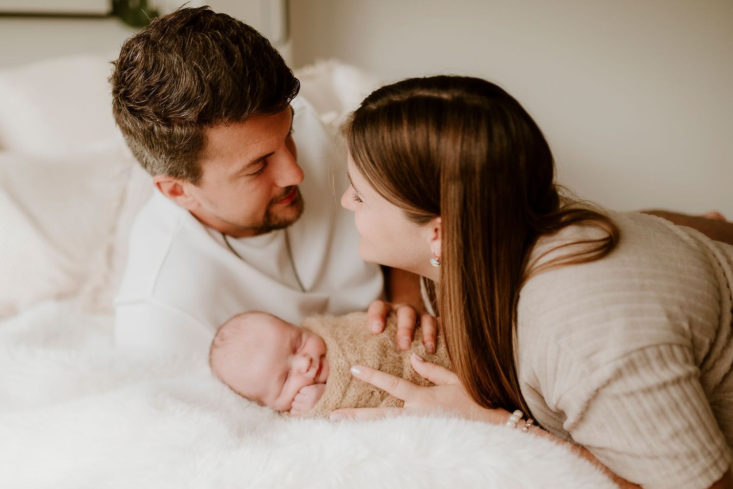 New parents gazing lovingly at their newborn baby during a soft, bright newborn photography session.