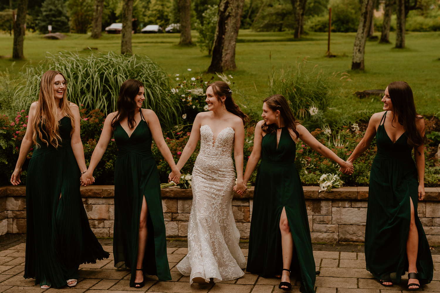 Bride in white gown poses with bridesmaids wearing black dresses on stone steps.
