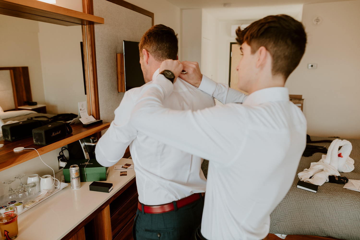 Men helping each other get ready, adjusting formal wear before event.