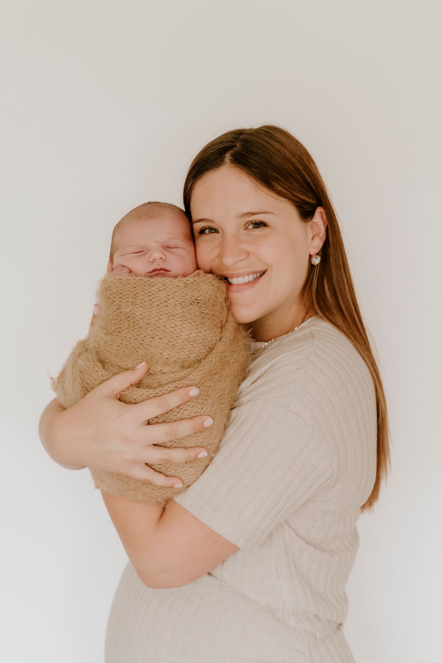 Happy mother holding her sleeping newborn baby wrapped in a burlap swaddle blanket.