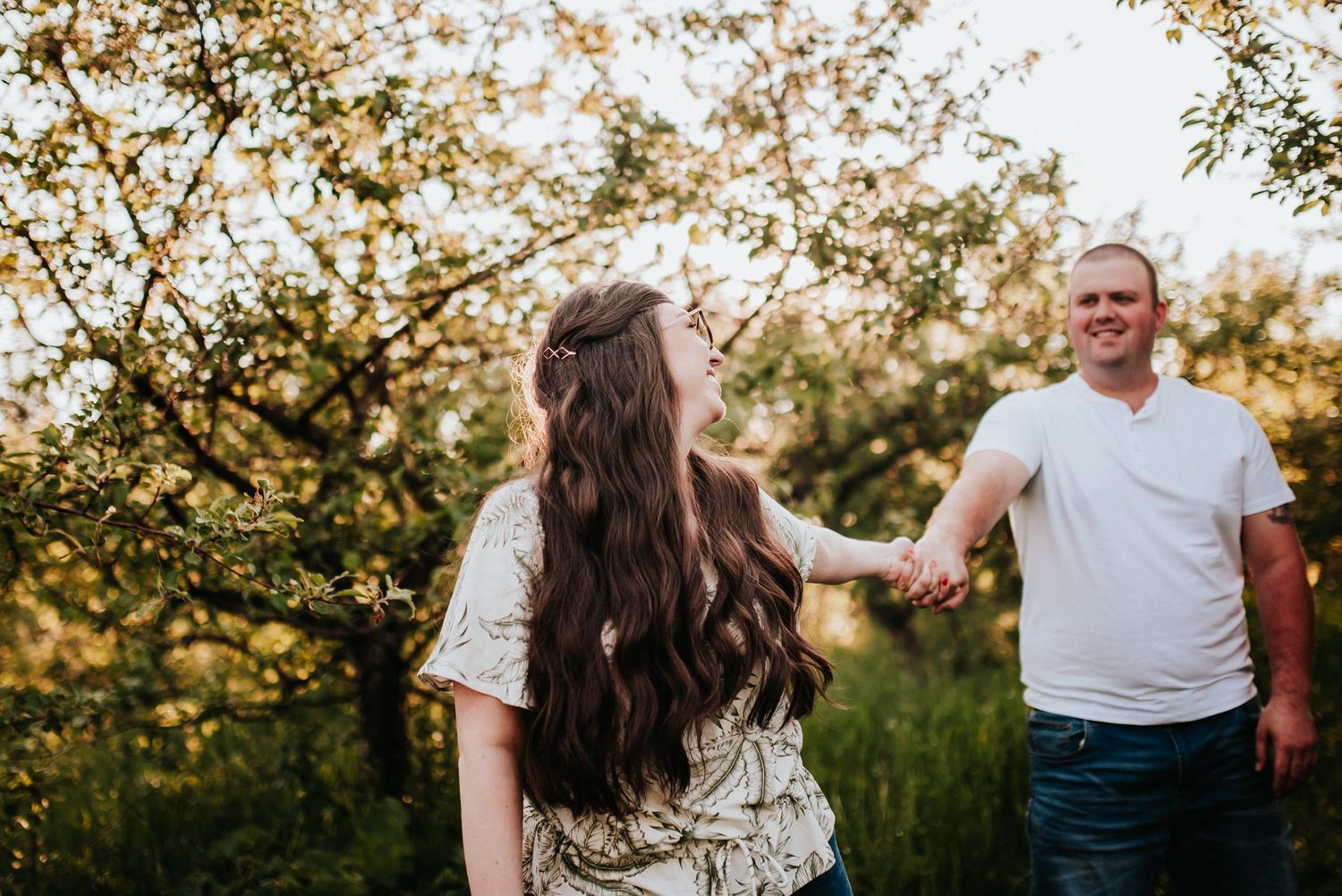 Couple walking hand in hand through beautiful sunlit orchard.