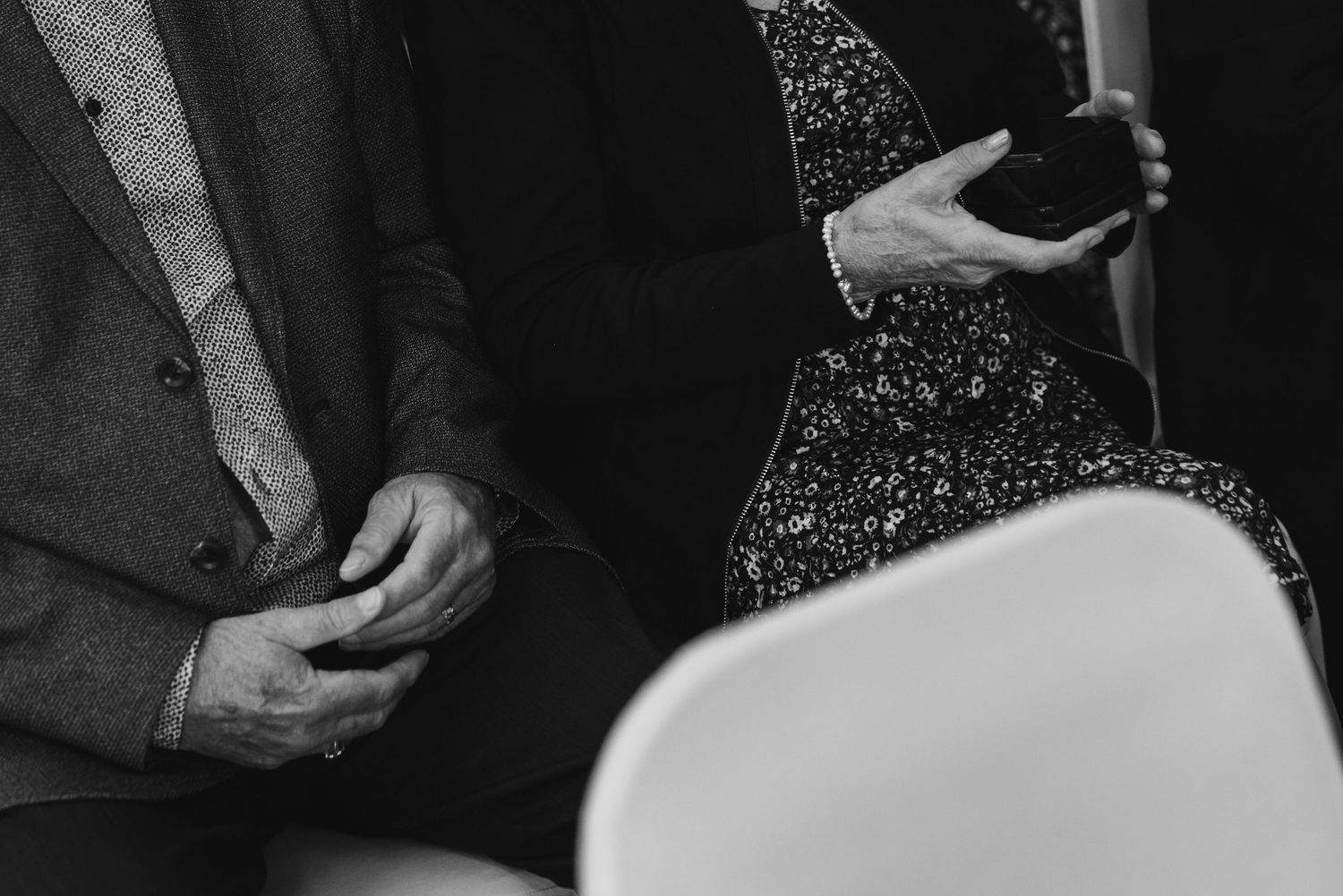 Black and white detail shot of hands and formal attire at wedding ceremony.