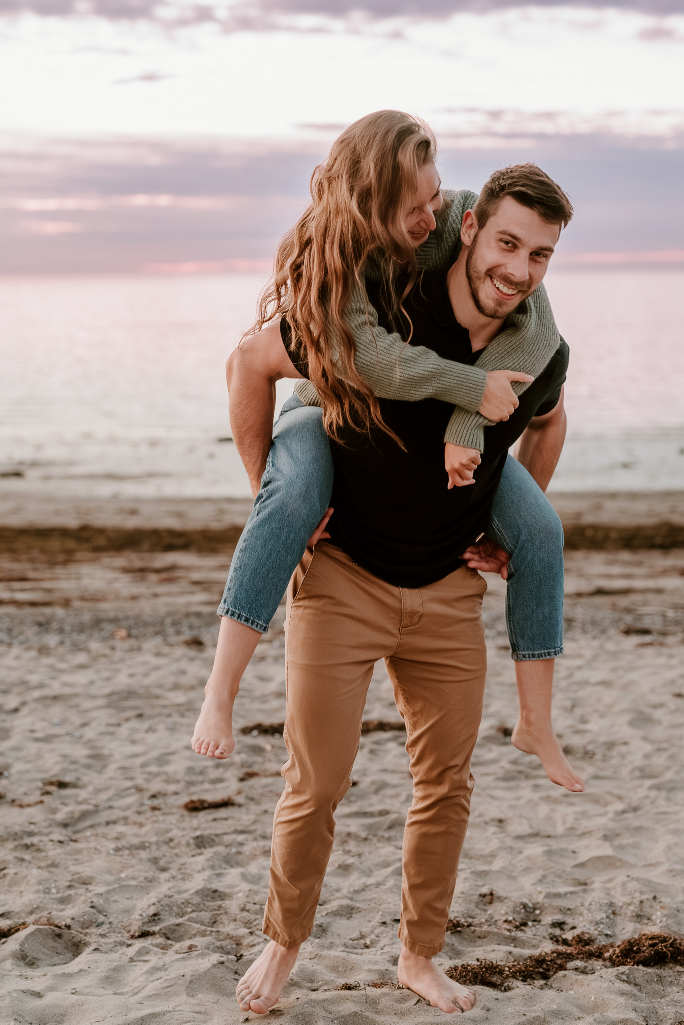 A playful couple shares joyful moments together on a sandy beach at sunset.
