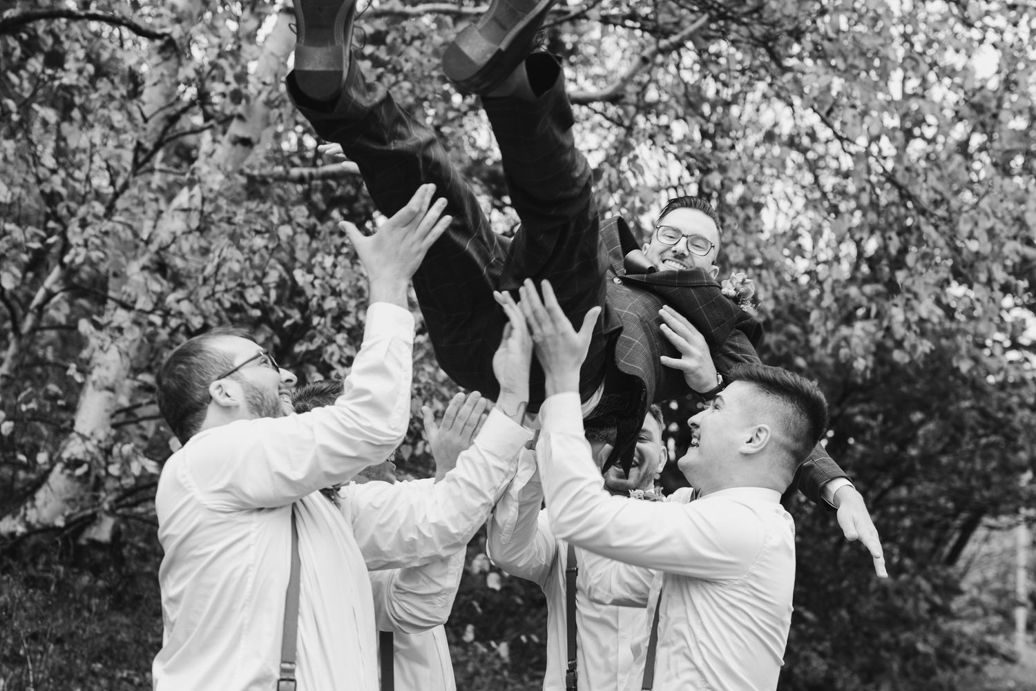 Groomsmen tossing someone in the air during playful wedding party photo session.