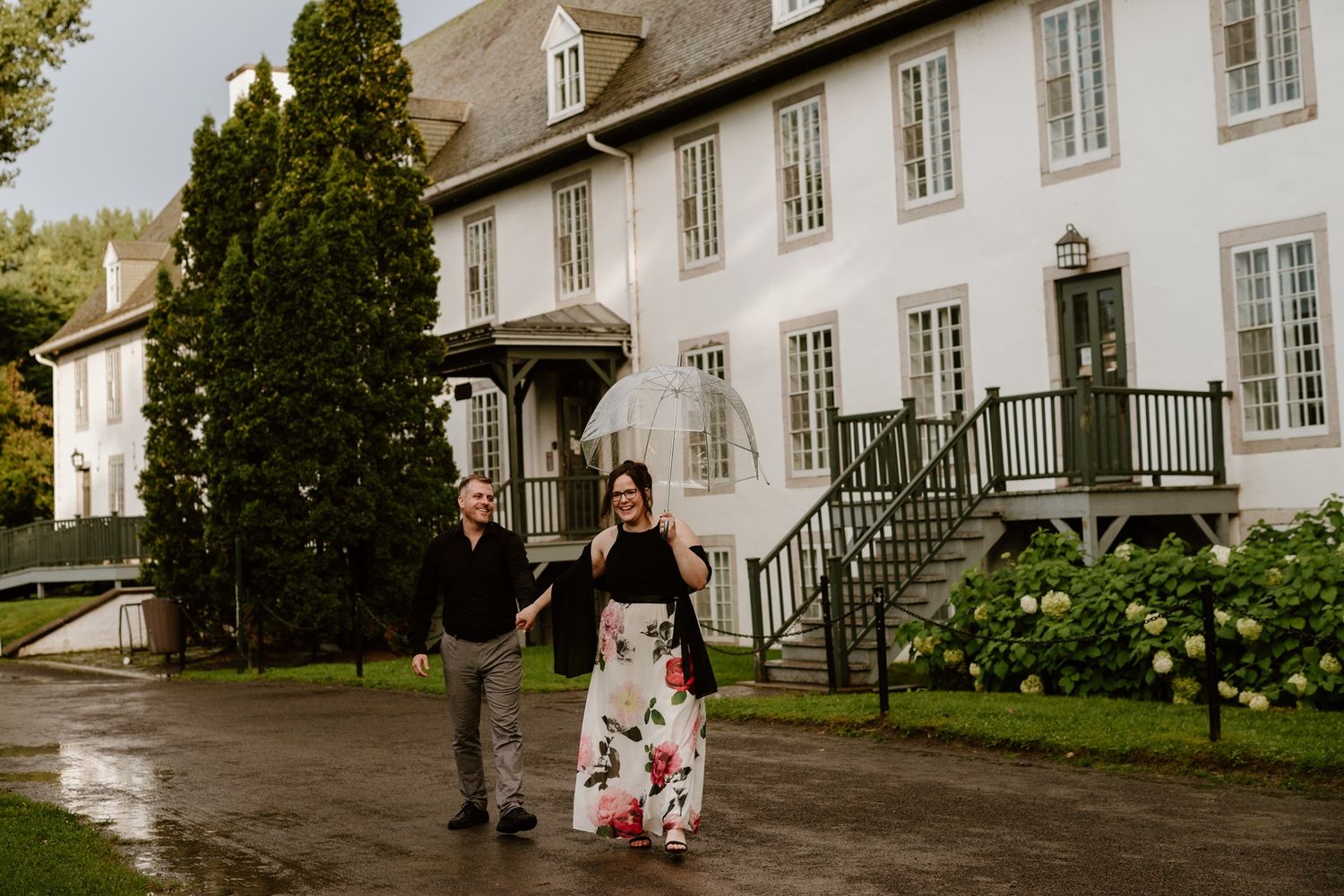 Couple walking together outside historic white building on rainy day.
