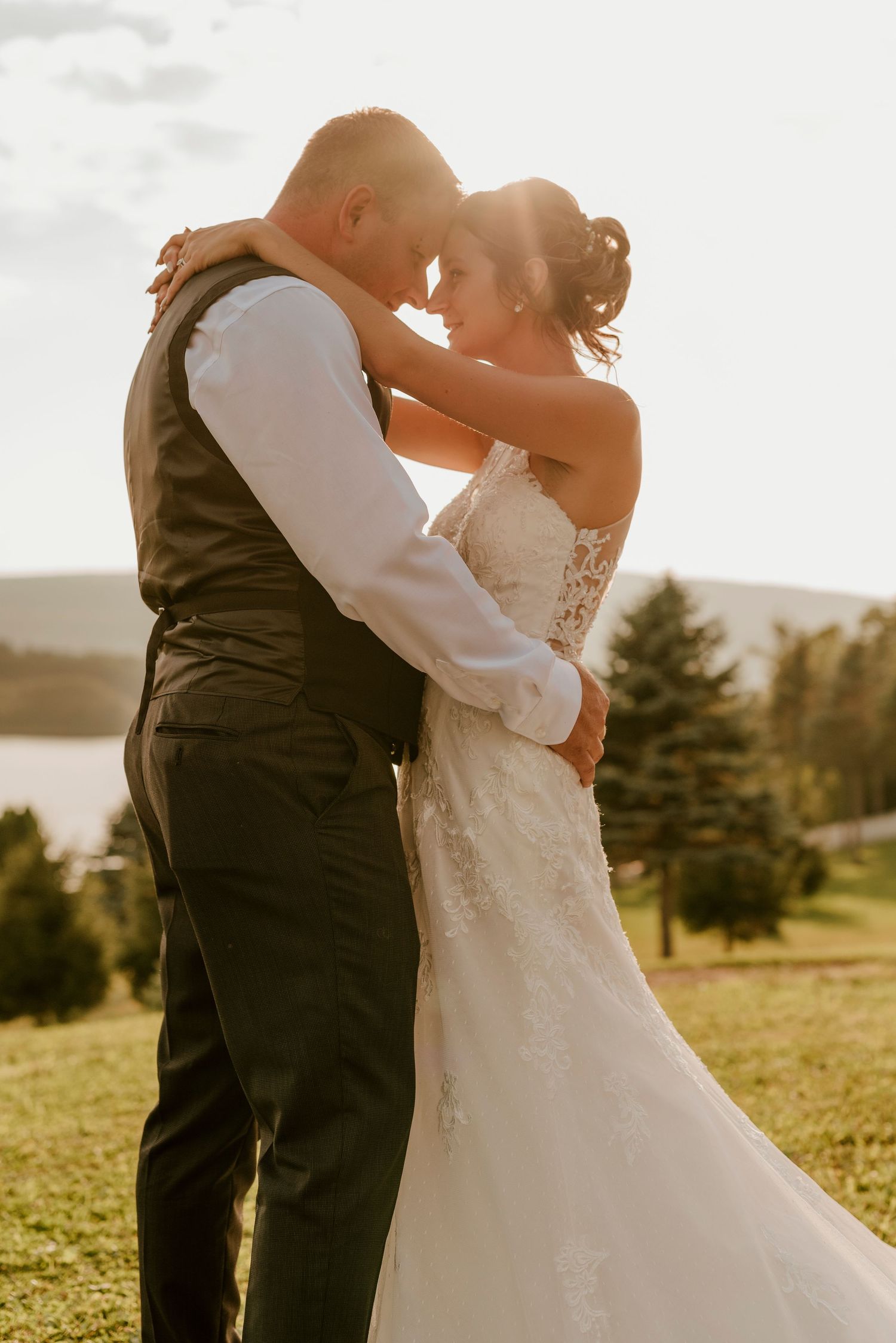 A romantic embrace between newlyweds on a hillside with a scenic lake view in the background.