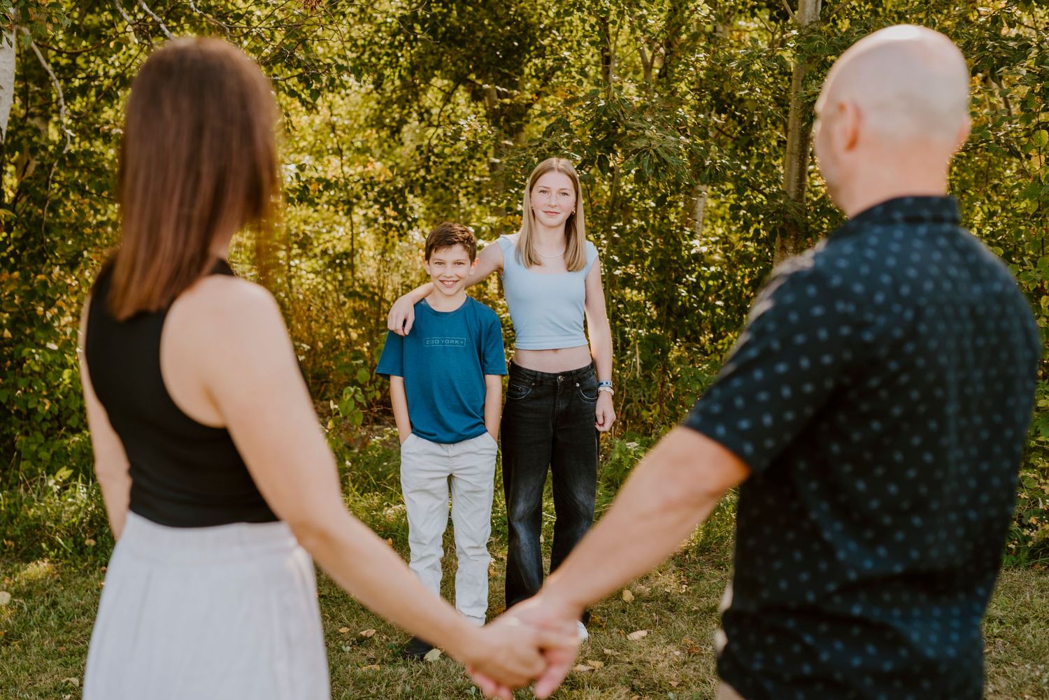 Deux enfants qui s'enlacent dans une lumière chaleureuse et leurs parents qui les regardent fièrement, main dans la main.