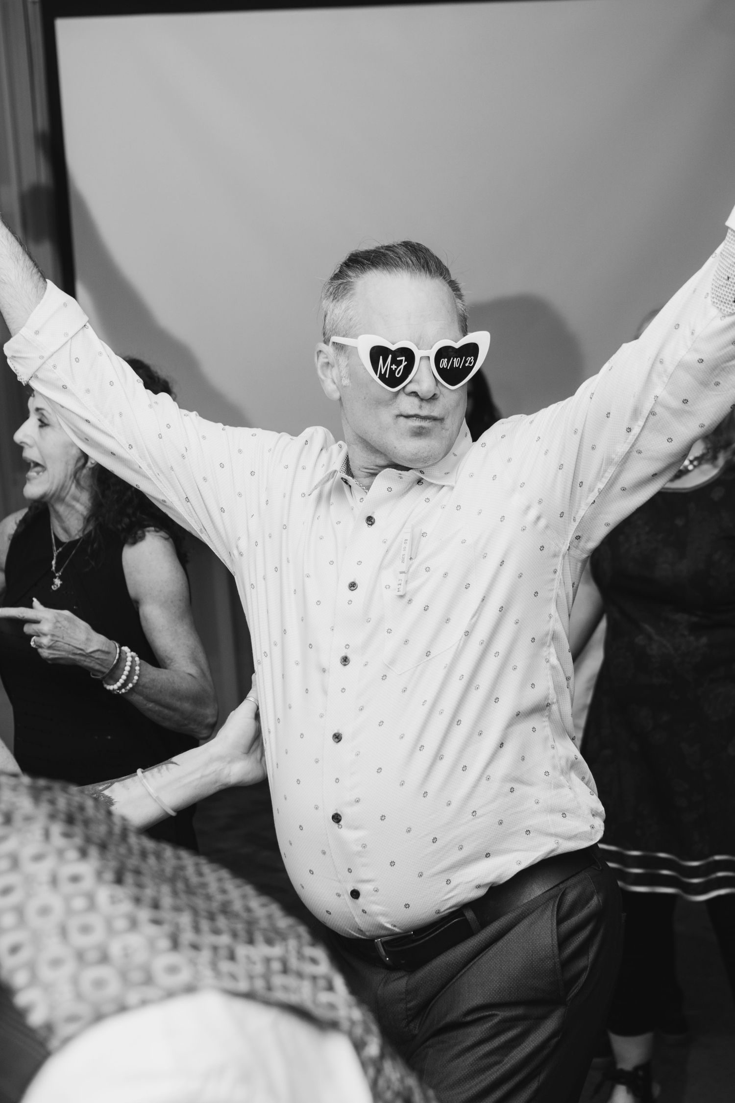 Wedding guest wearing heart-shaped sunglasses dances enthusiastically at reception celebration.
