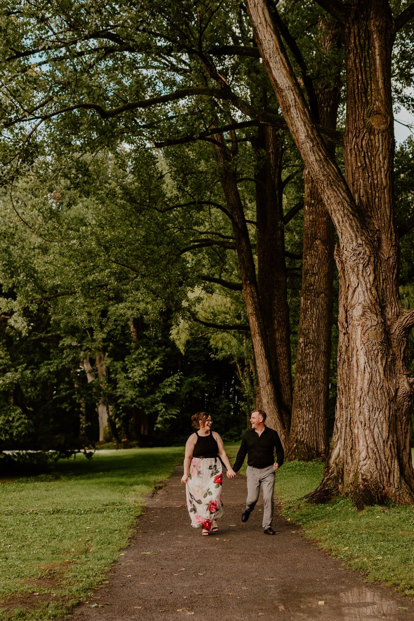 Couple walking hand in hand down tree-lined path in summer garden.