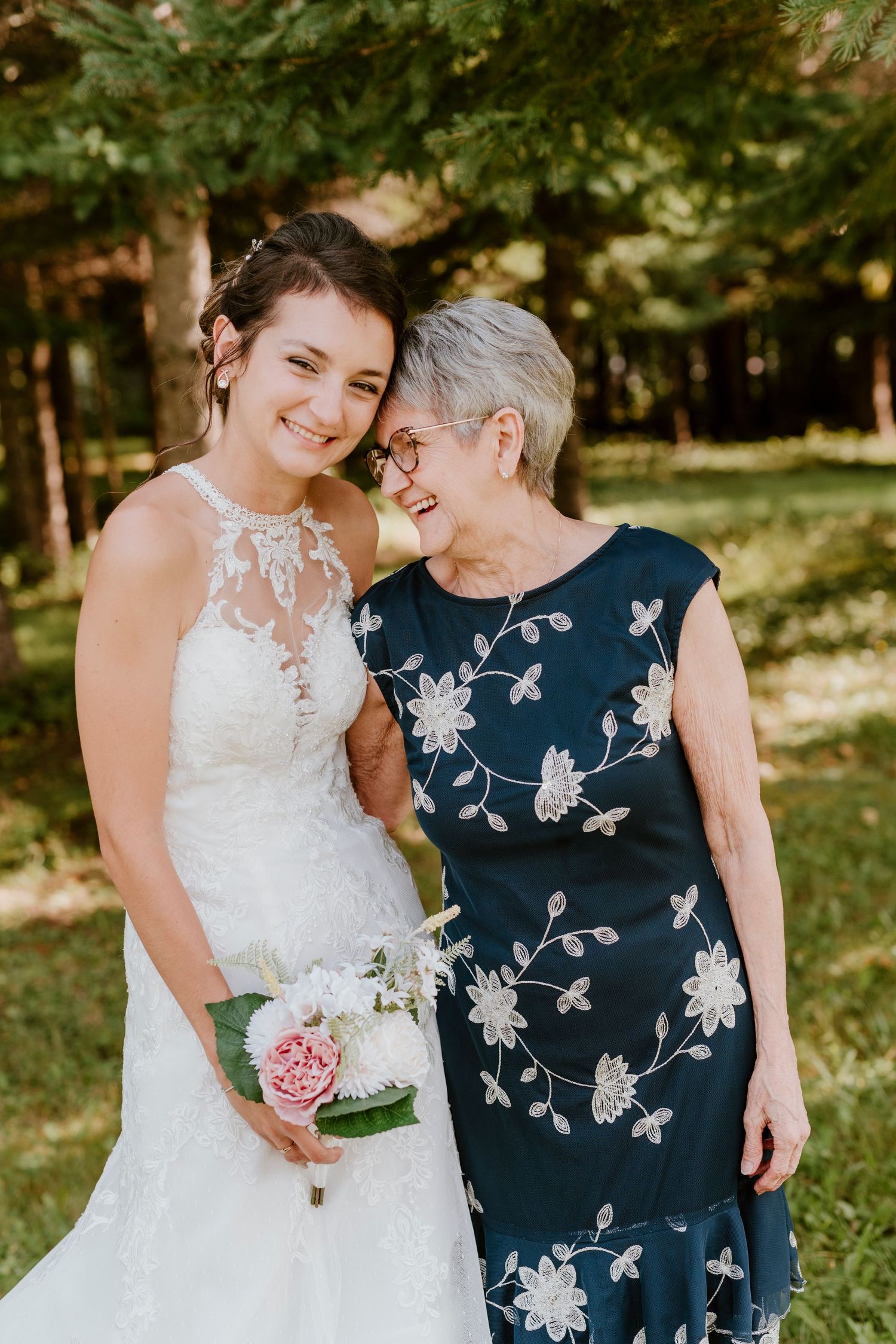Touching moment shared between bride in lace dress and guest wearing floral navy dress.