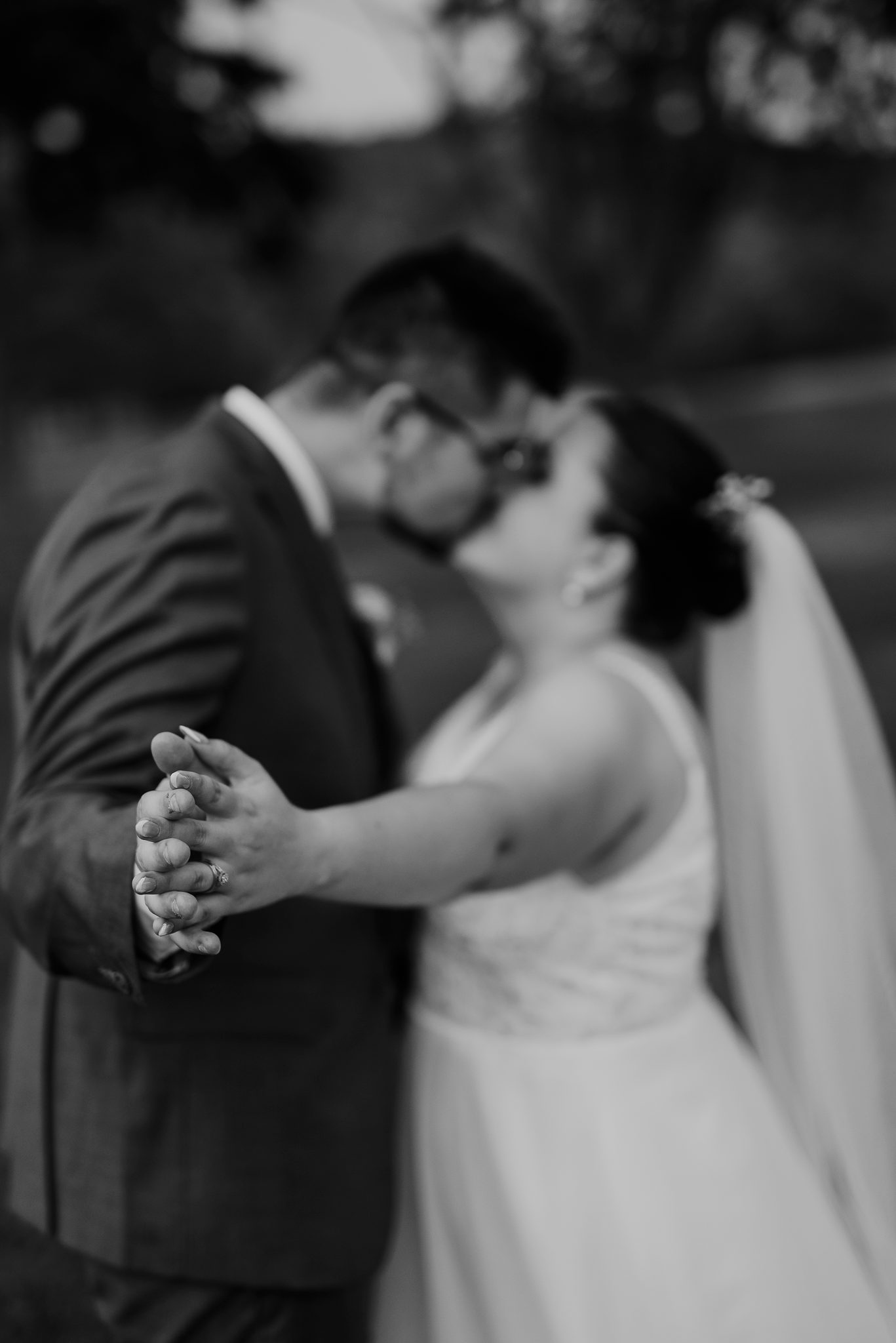 A black and white wedding photo capturing a romantic dance with clasped hands in the foreground.