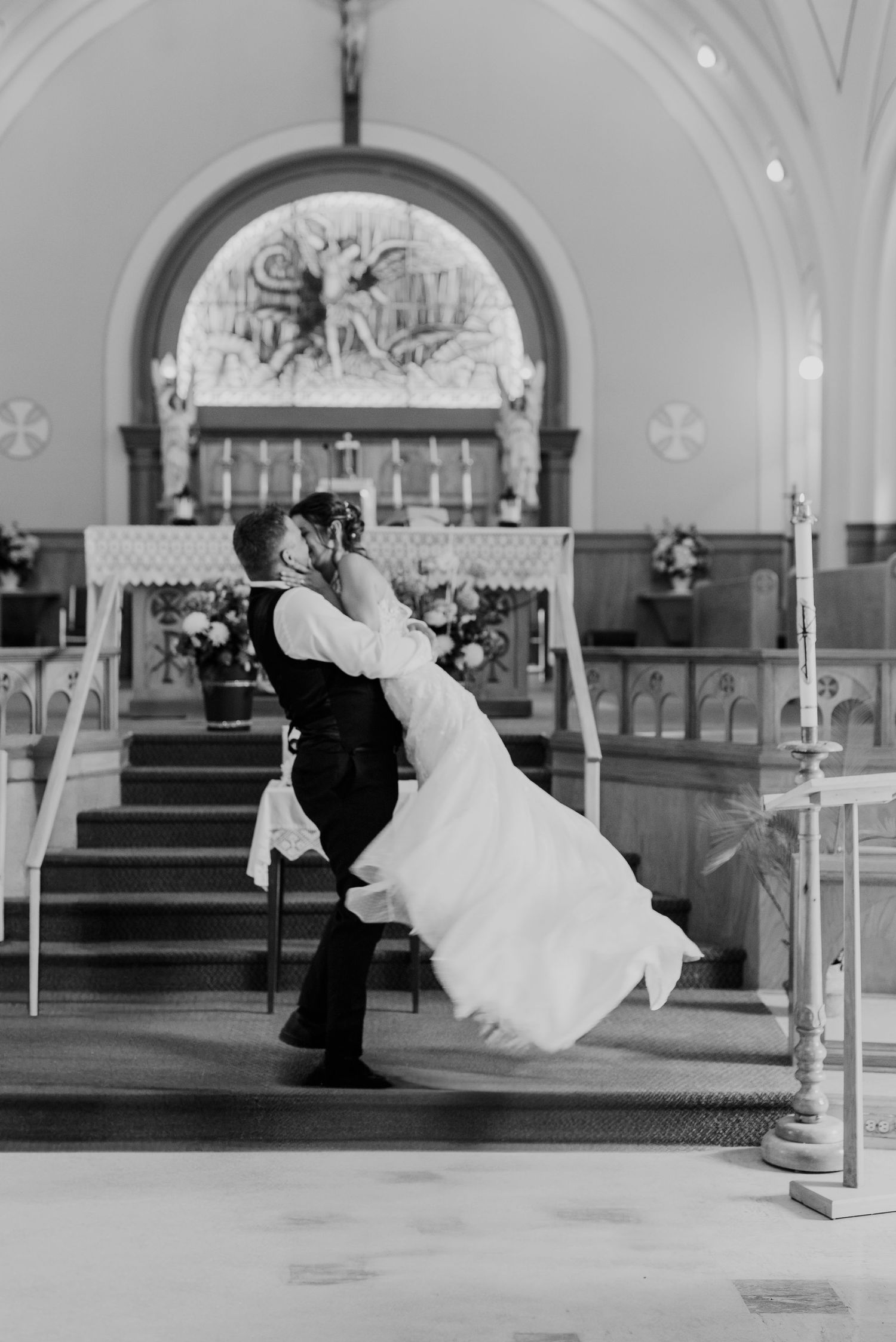 Dramatic black and white photo of newlyweds dancing in church with elegant architectural details.