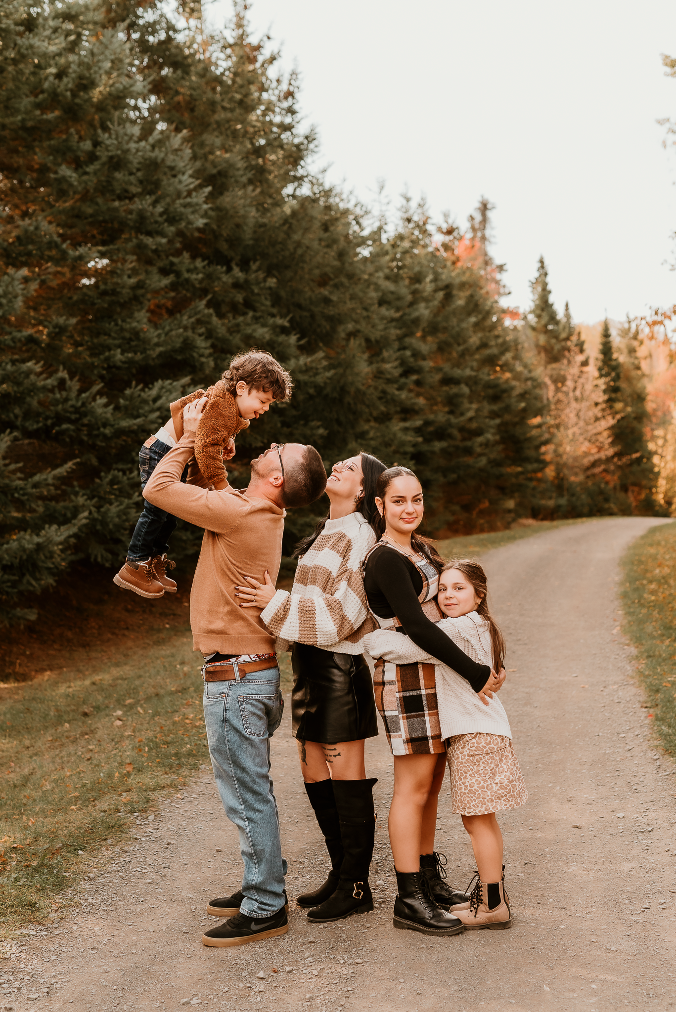 Family of five posing on a scenic autumn path surrounded by evergreen trees during a fall outdoor photo session.