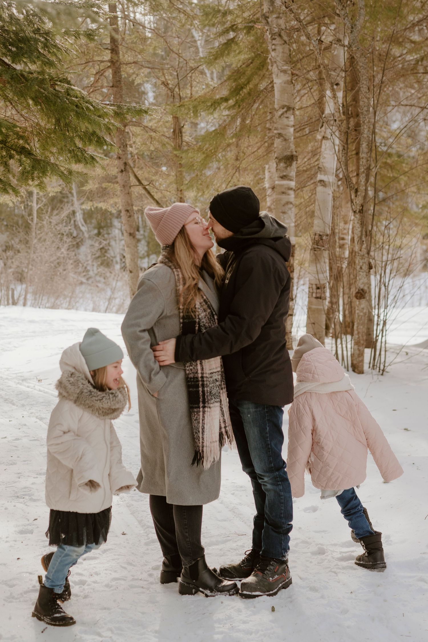 Winter family portrait in snowy forest with children bundled up in warm coats.