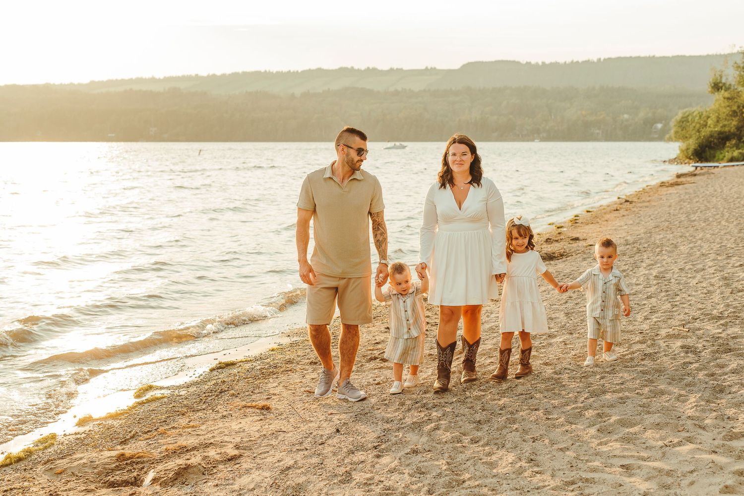 Family of five walking hand-in-hand along a sandy beach at golden sunset hour.