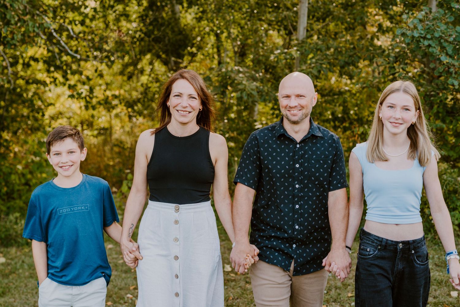 Dans un cadre estival et chaleureux, les quatre membres d'une famille se tiennent la main.