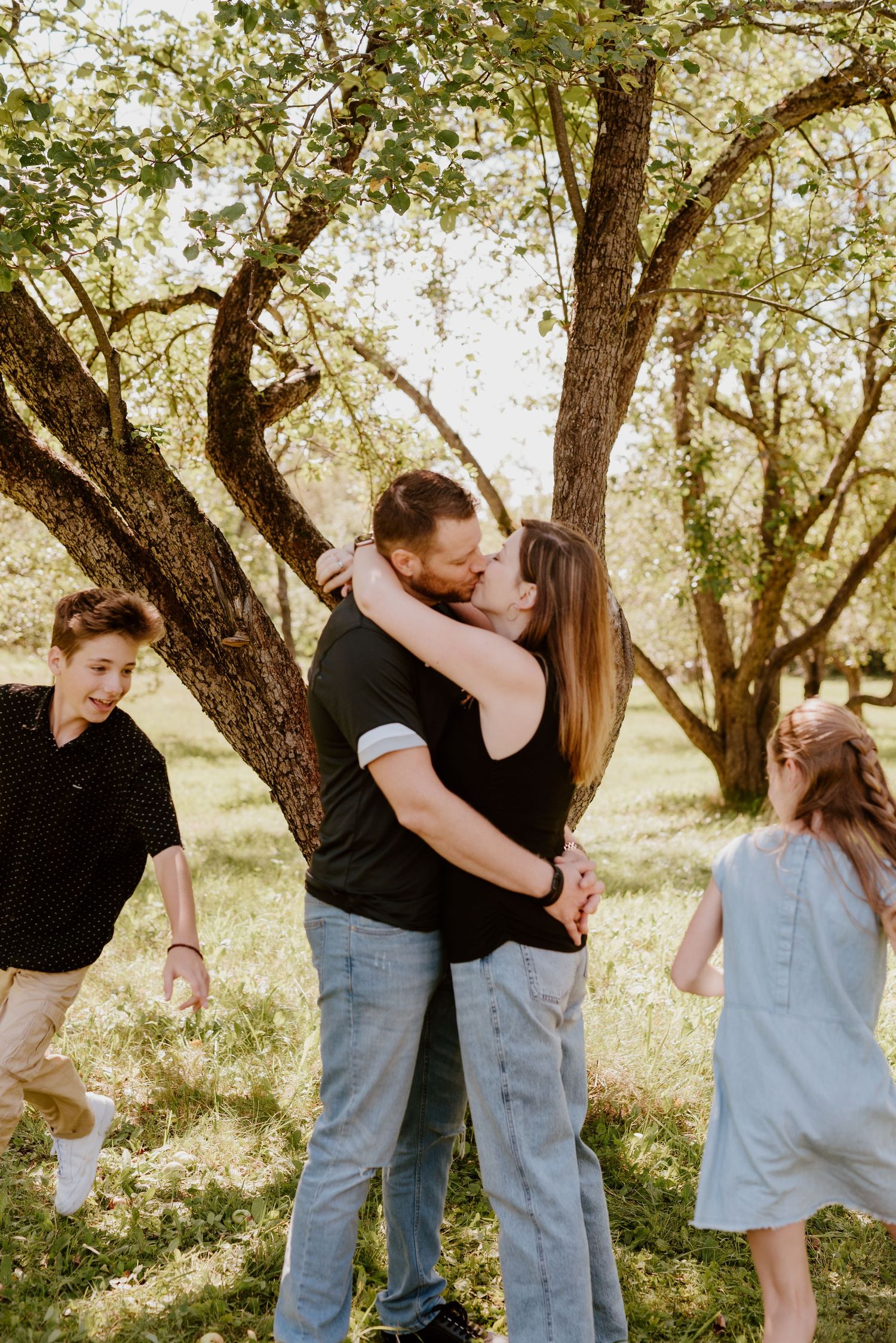 Devant un arbre majestueux, un couple, entouré de leurs deux enfants qui jouent, s'embrasse tendrement.