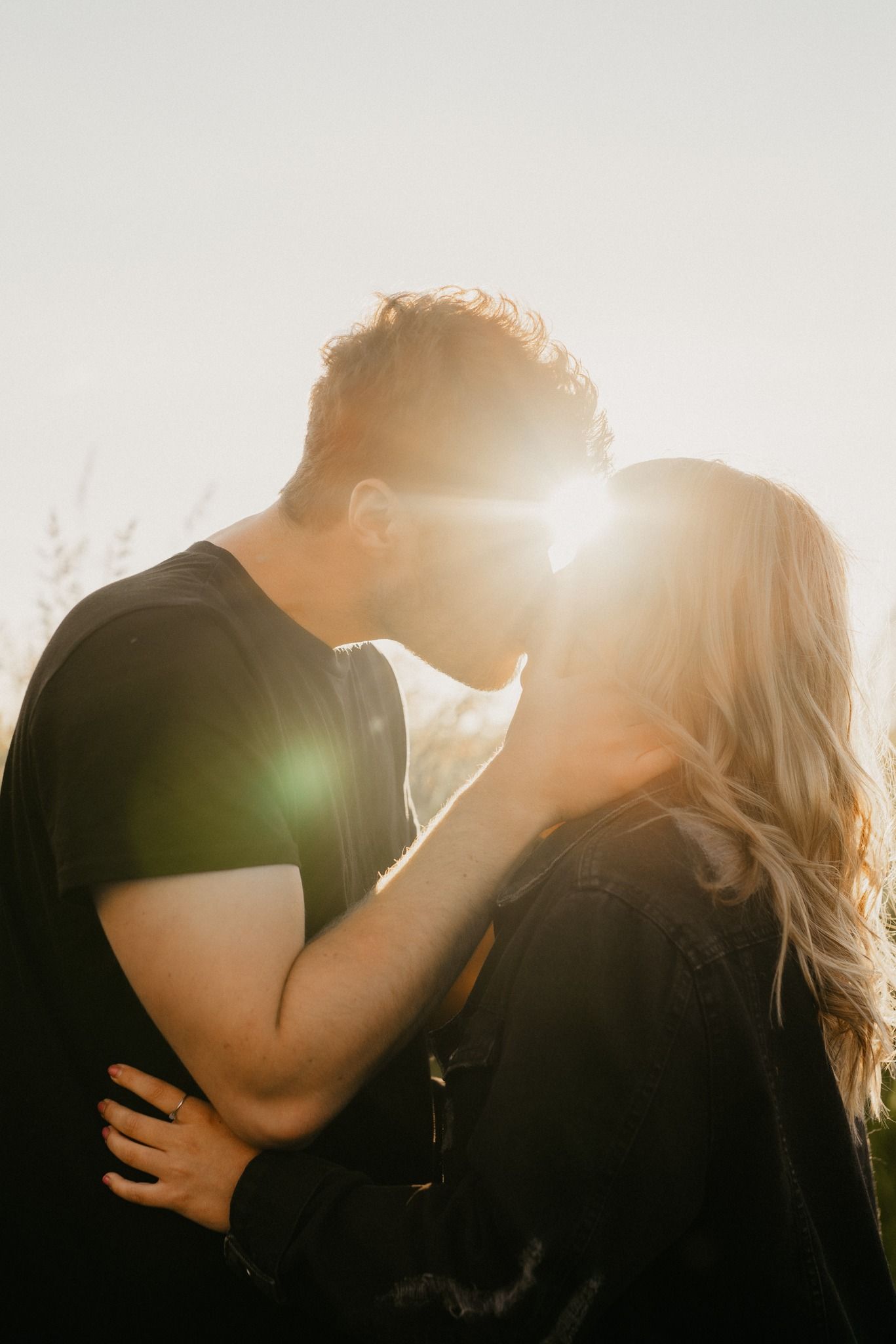 Silhouetted couple sharing intimate moment with sun flare in background.