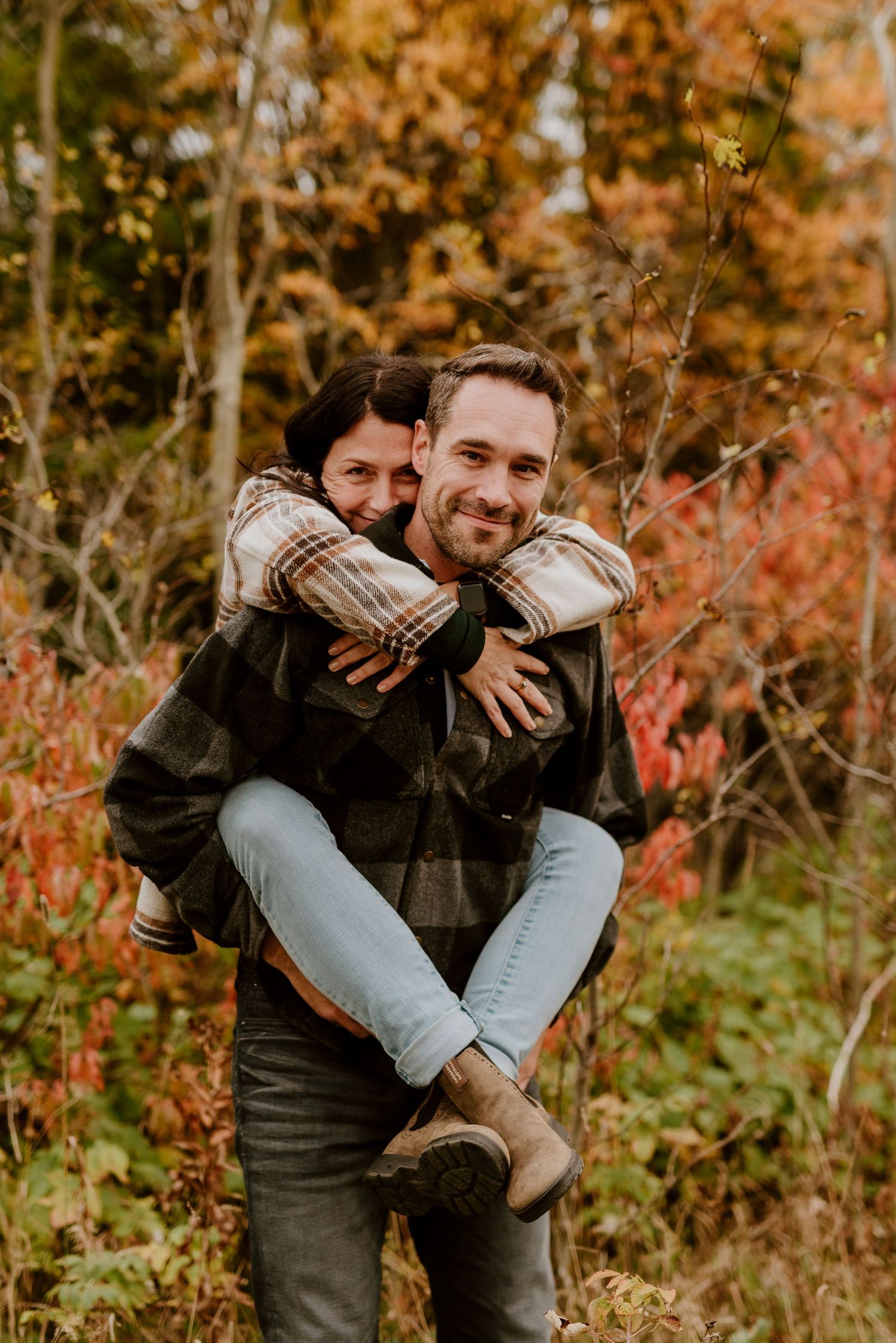Cozy piggyback moment against colorful fall forest background.