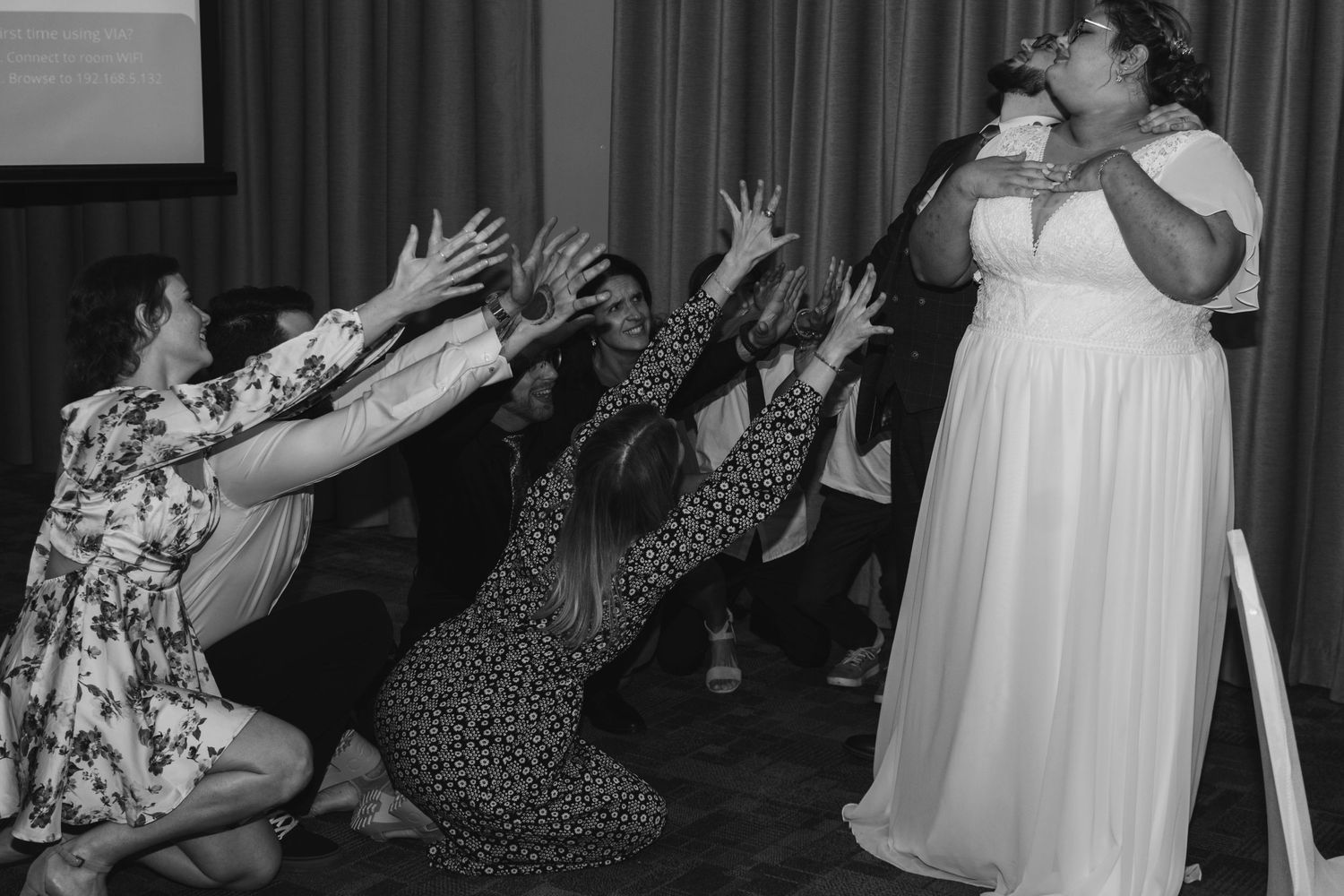 Wedding guests excitedly dancing and reaching towards a performer at a reception.