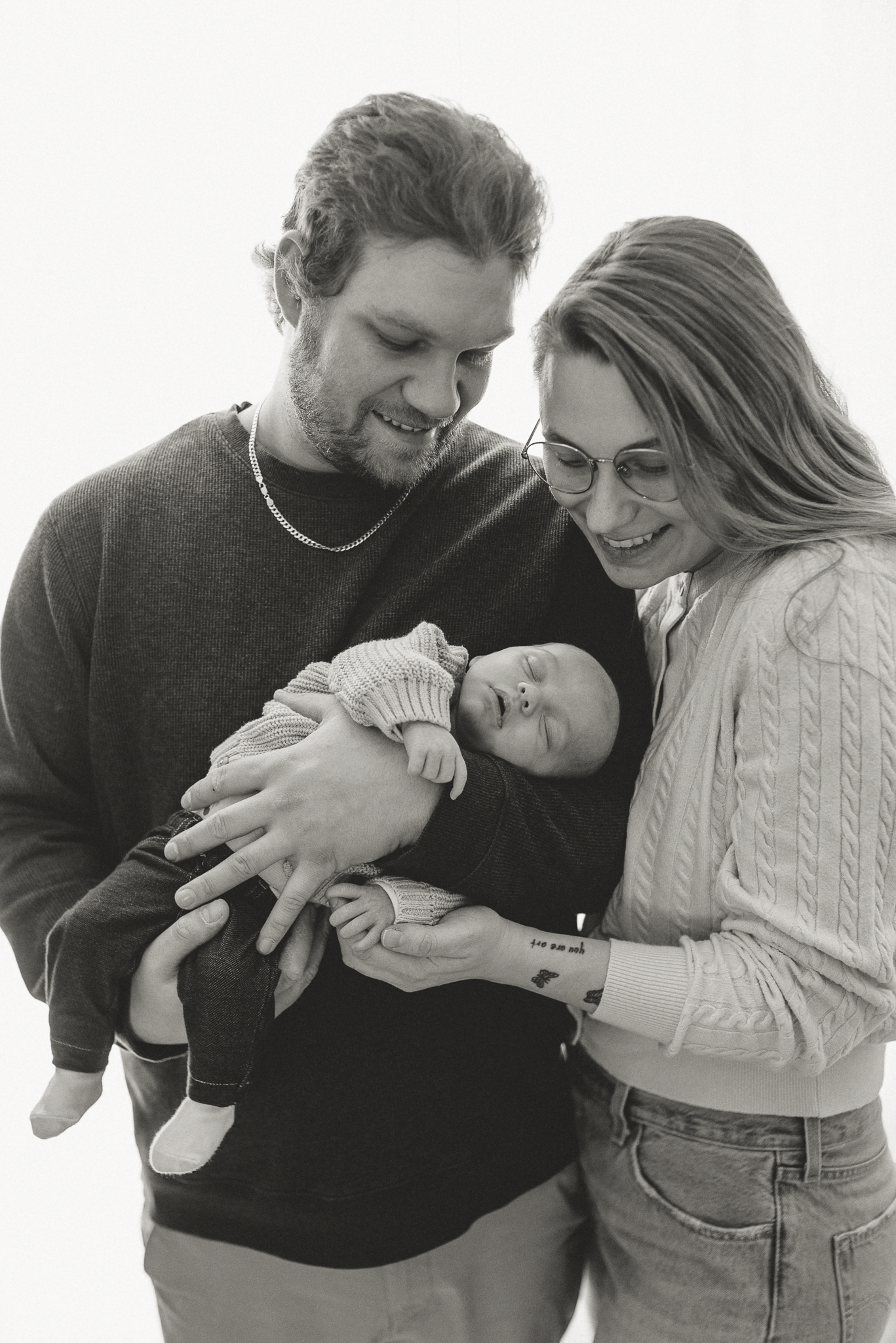 Black and white photo of smiling parents holding their newborn baby, family portrait studio photography.