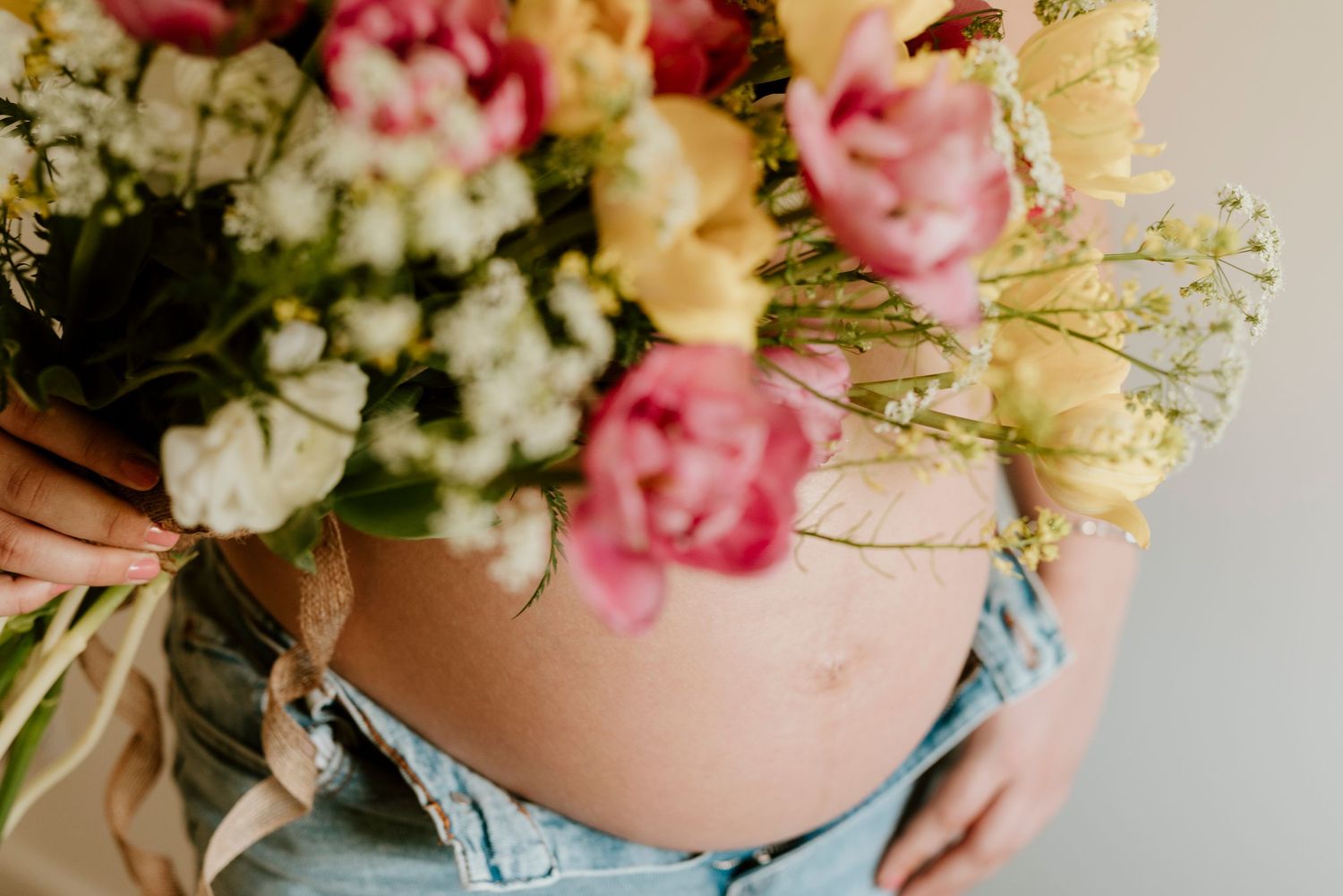 Pregnant belly in denim with delicate pink and white flowers arranged on top in a romantic maternity photo.