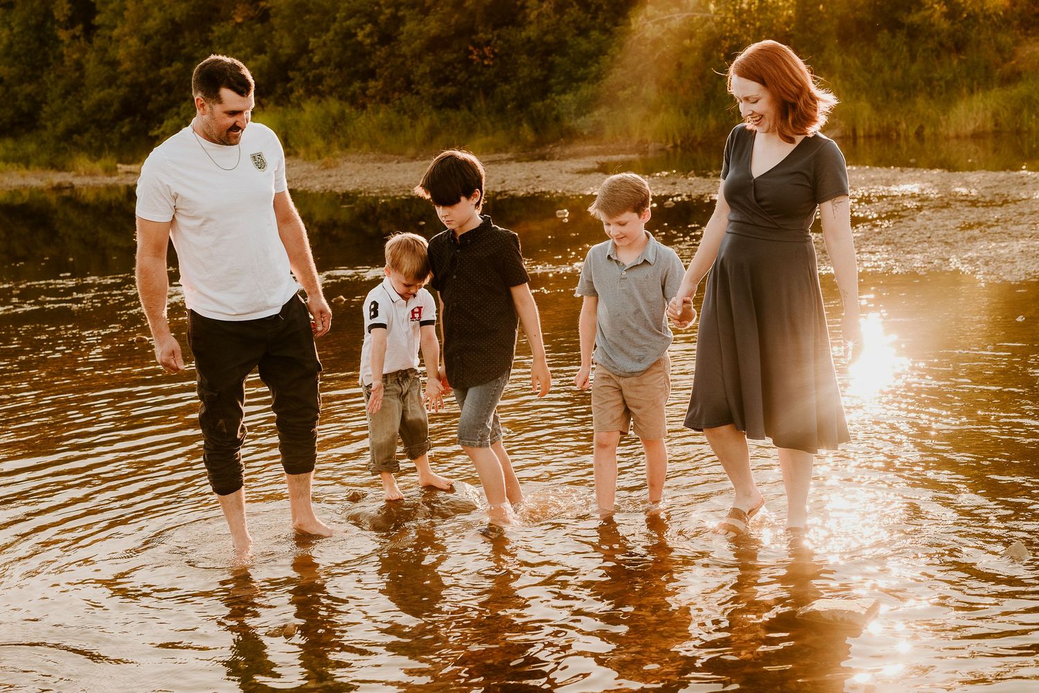 A group of people wading in shallow water at sunset, creating ripples as they walk along the shoreline together.