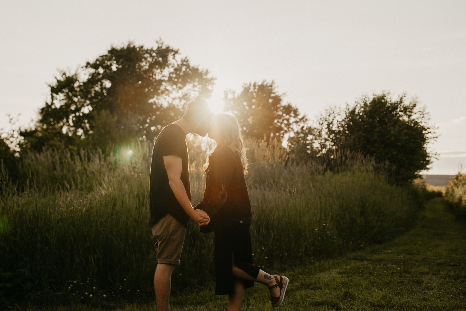 Couple standing in tall grass field at sunset with pet dog.