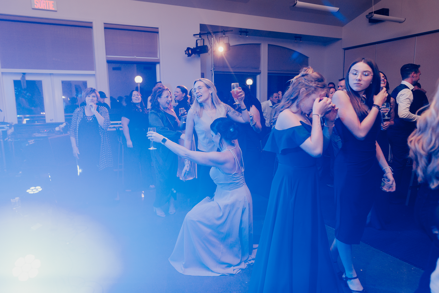 Wedding reception dance floor filled with guests dancing under blue lighting.