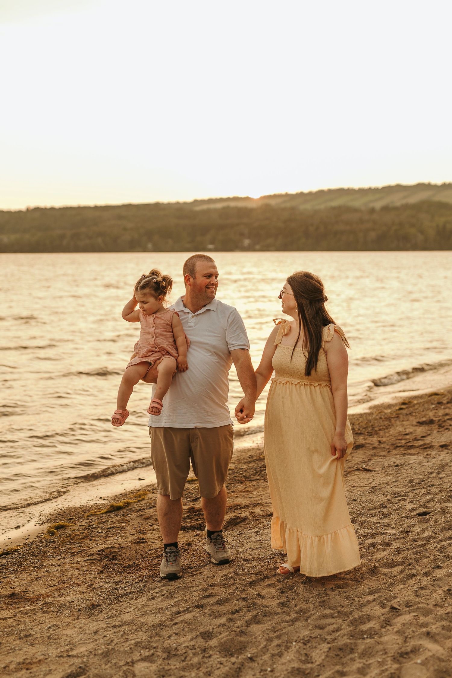 A family walks together along a sandy beach at sunset, creating silhouettes against the golden water.