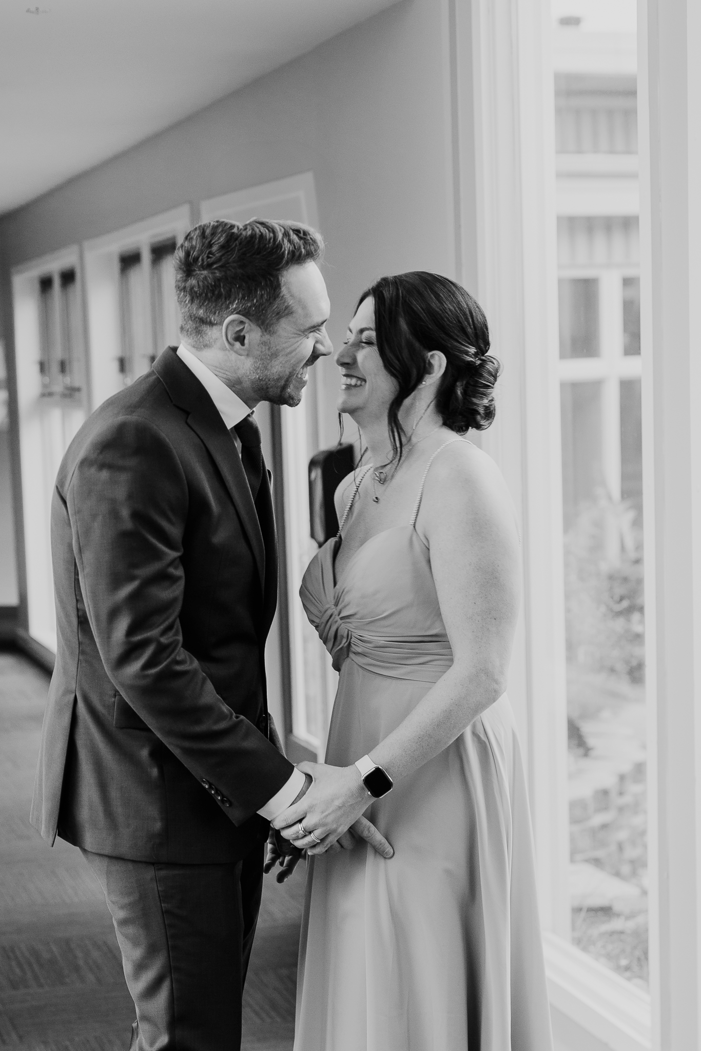 Intimate black and white portrait of couple sharing romantic moment by window.