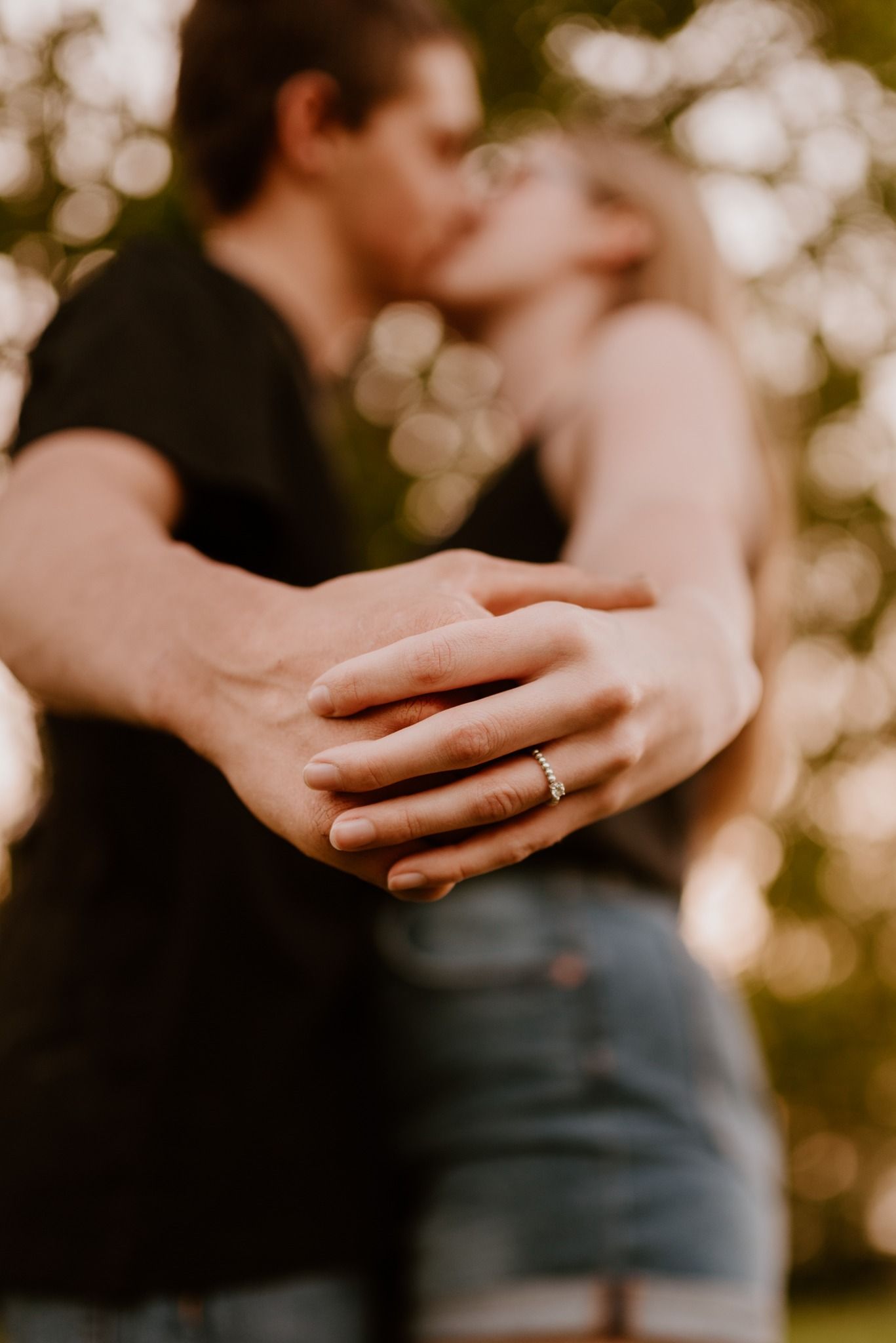Close-up of hands with wedding ring as couple shares romantic moment in golden sunlight.