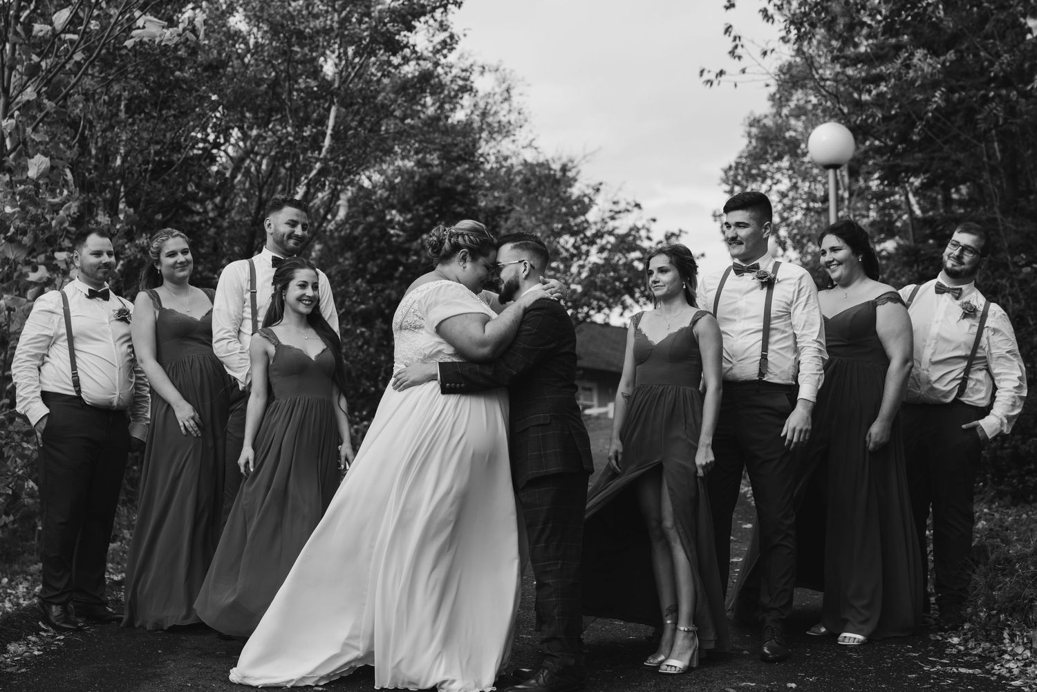 Wedding party gathered around couple for celebratory photo outdoors.