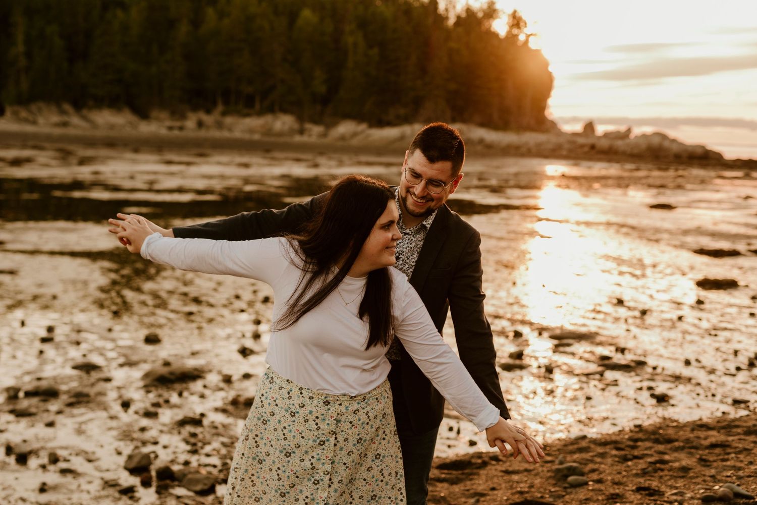 Playful couple dancing on beach shore during golden hour sunset.