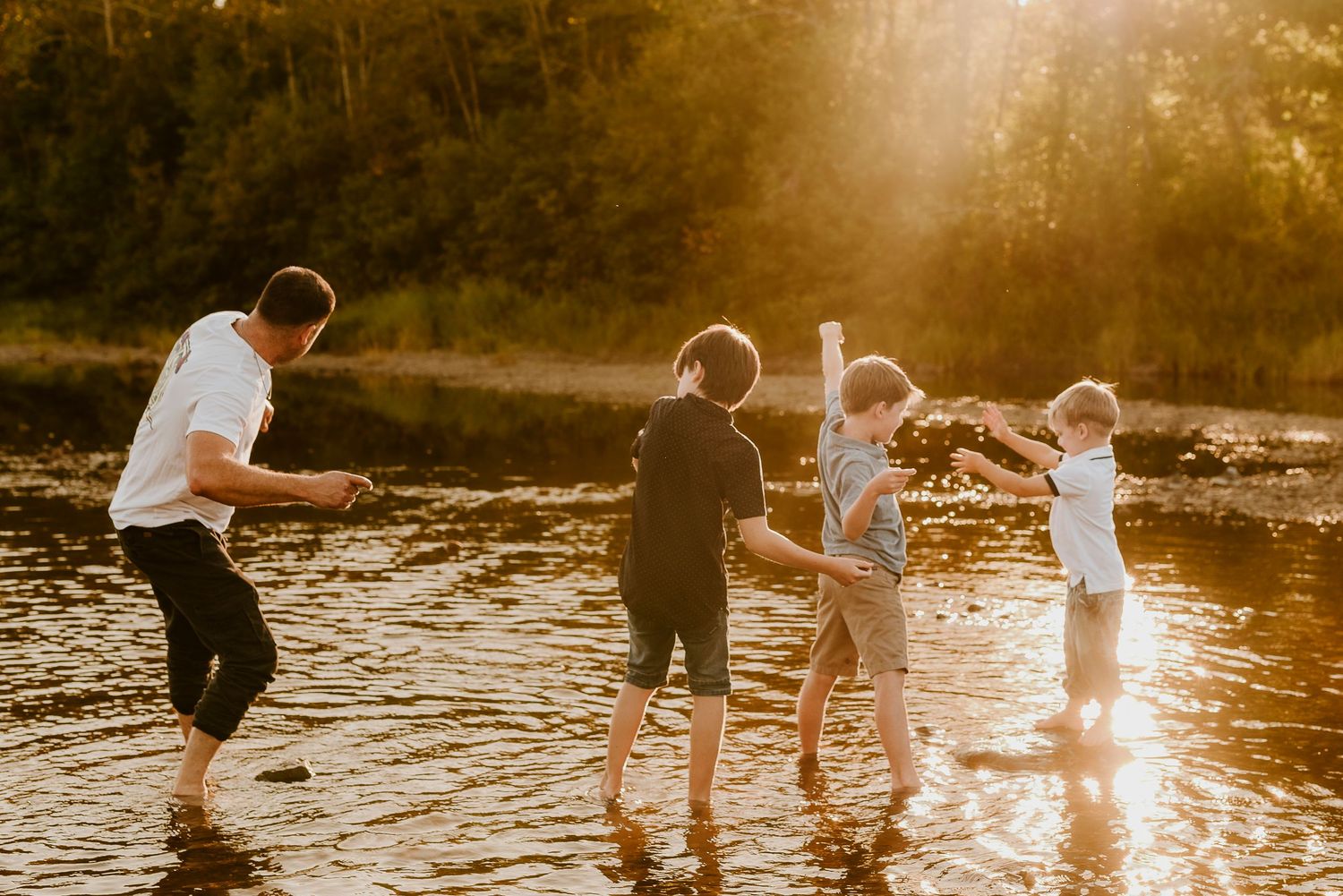 Family playing and splashing together in a golden sunlit lake during sunset creating joyful silhouettes.