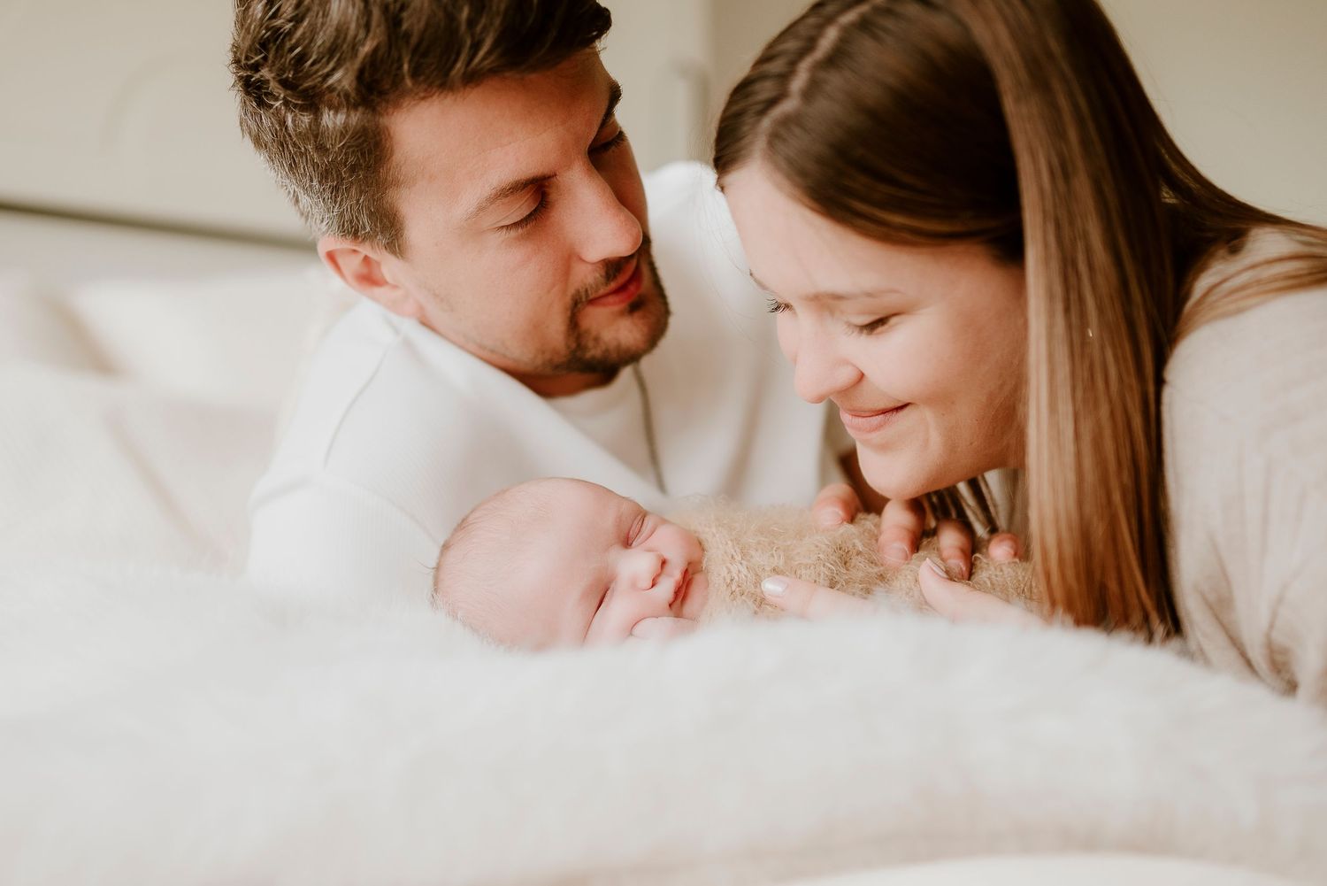 Happy parents lovingly gazing at their newborn baby wrapped in a soft blanket.