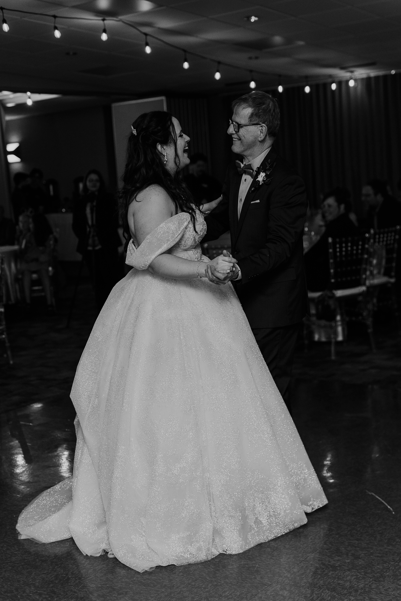A couple shares their first dance at their wedding reception under string lights.