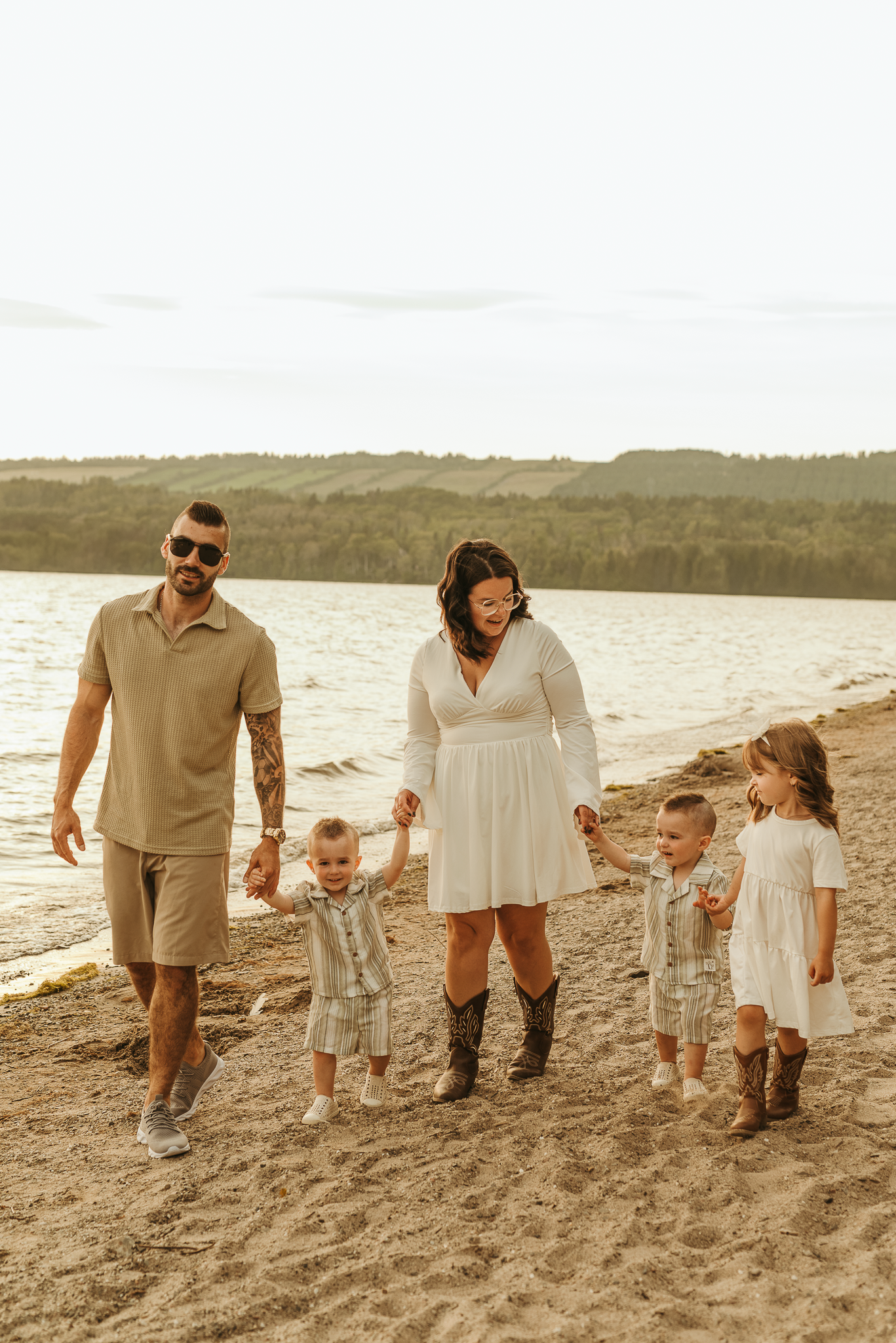 Family walking together on a sandy beach in neutral earth-toned outfits during sunset.