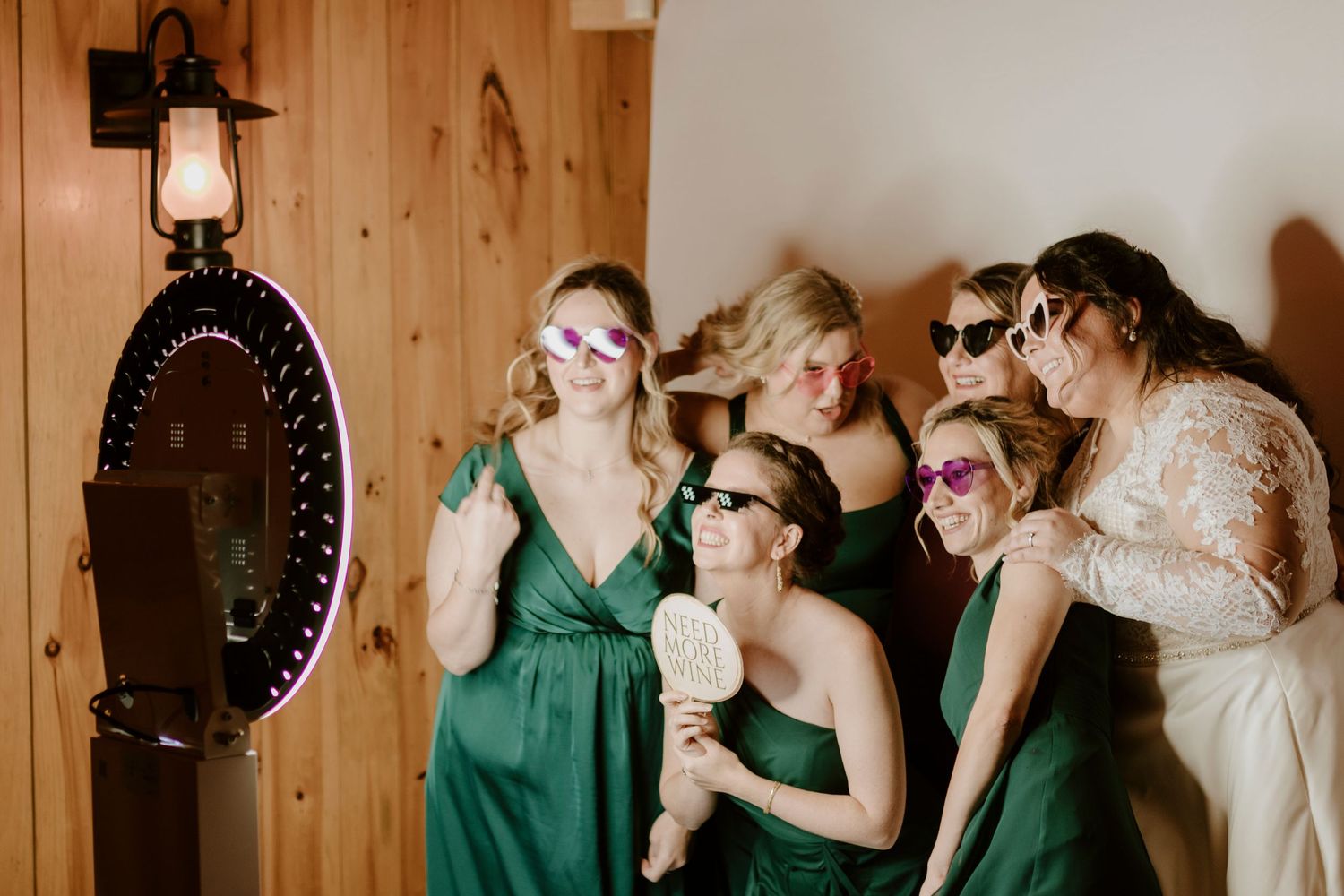 Bridesmaids in green dresses pose with fun sunglasses and props at a wedding photo booth.