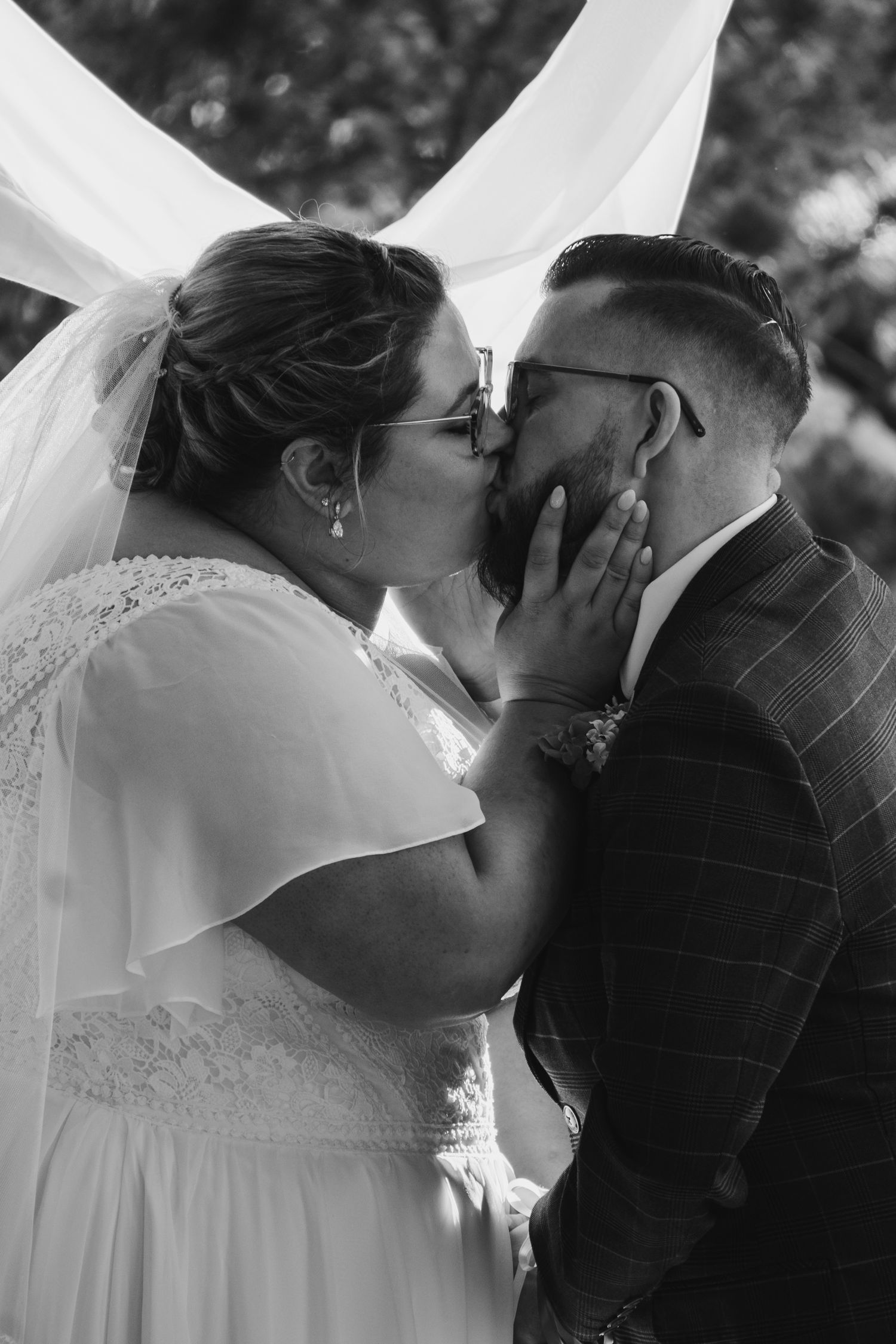 Romantic wedding kiss under white fabric arch in black and white photography.