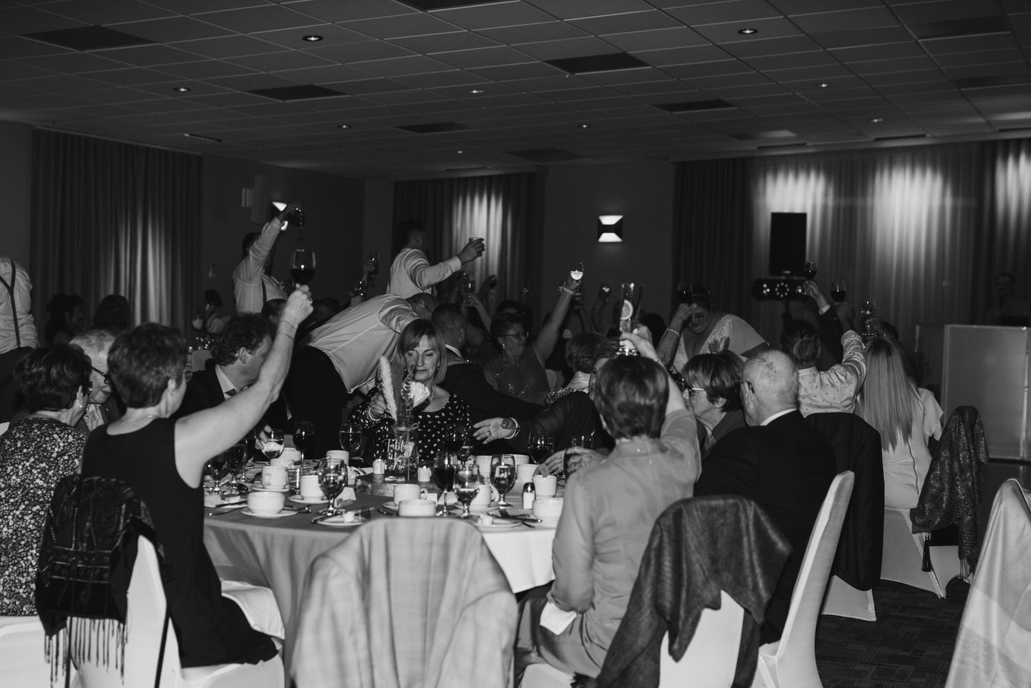 Black and white photo of guests dancing with hands raised at a wedding reception.