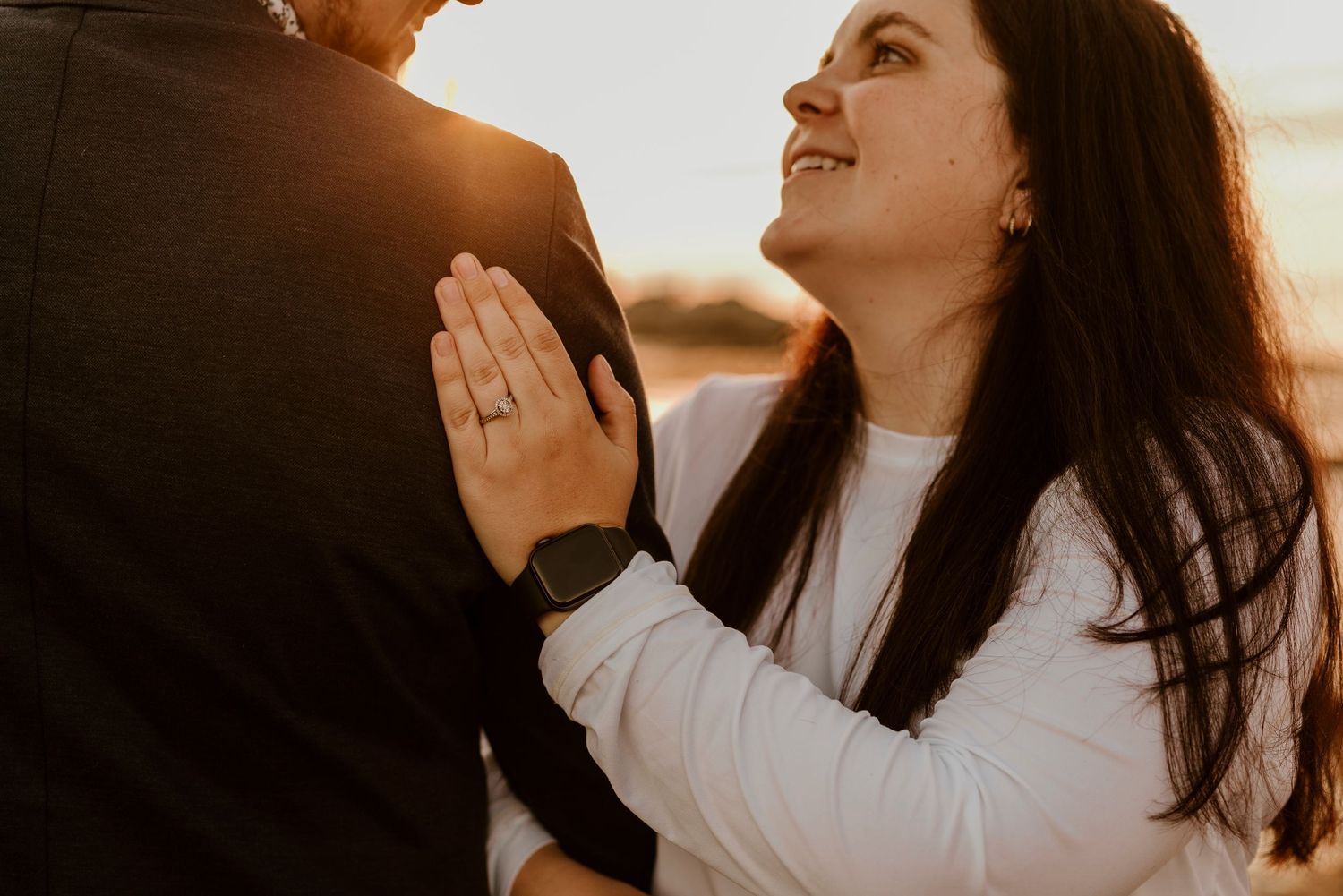 Couple embracing during sunset proposal moment showing off engagement ring.