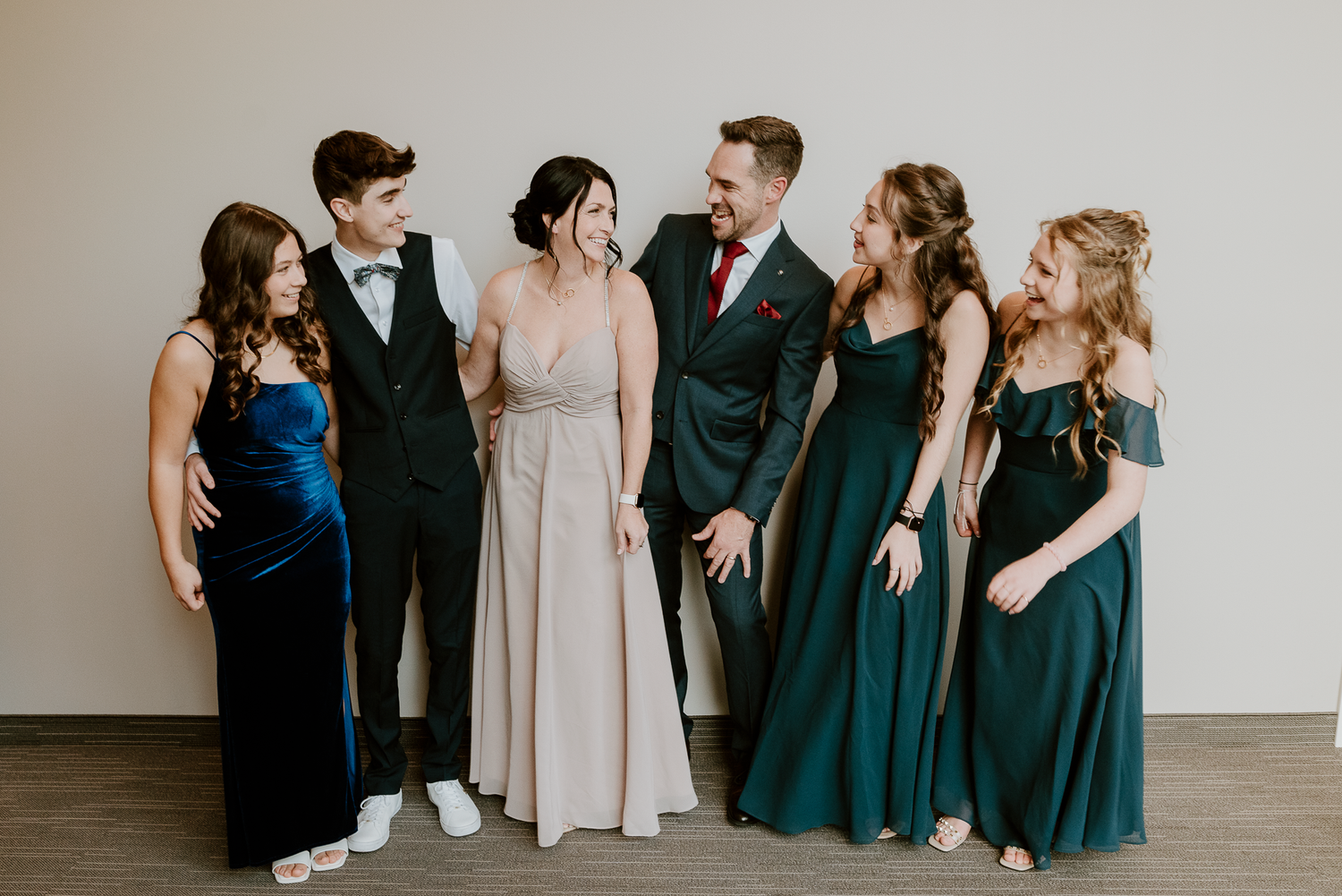 Wedding party poses together in formal attire with mix of navy and forest green dresses.