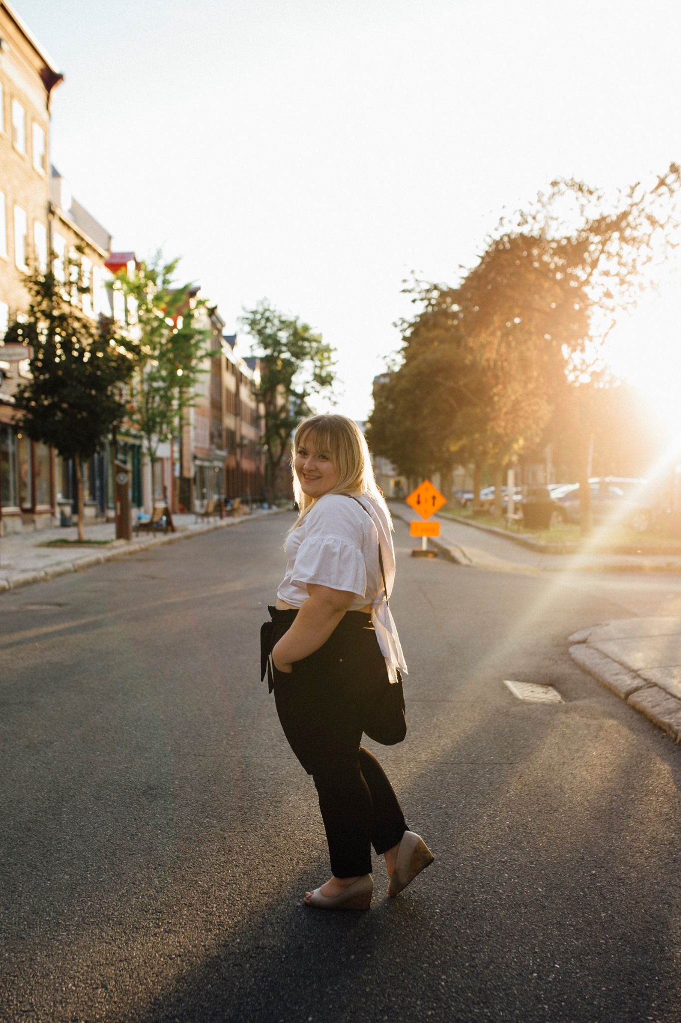Person posing on a city street during sunset with warm golden light.
