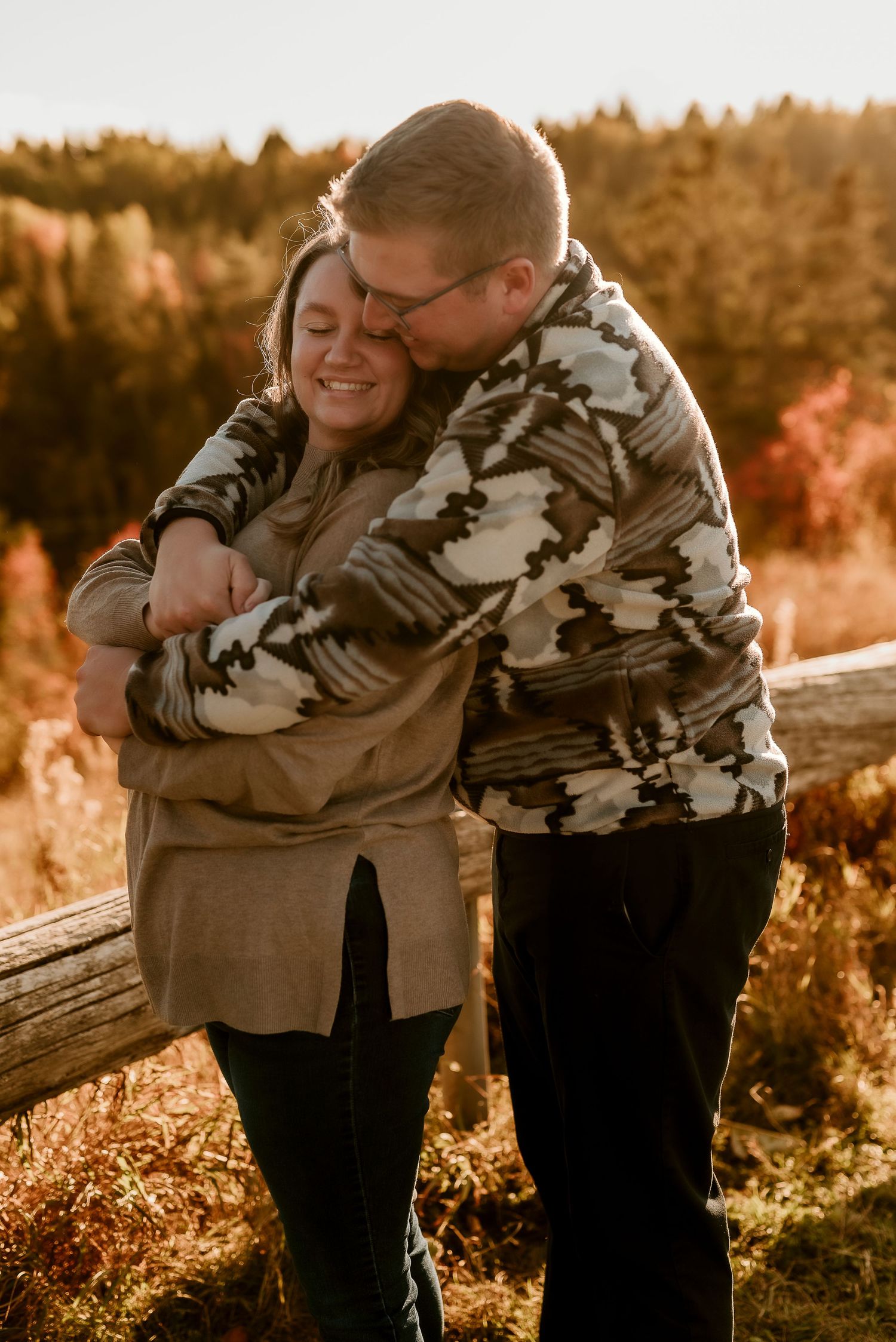 A couple shares tender embraces at sunset in a natural outdoor setting with golden light filtering through trees.