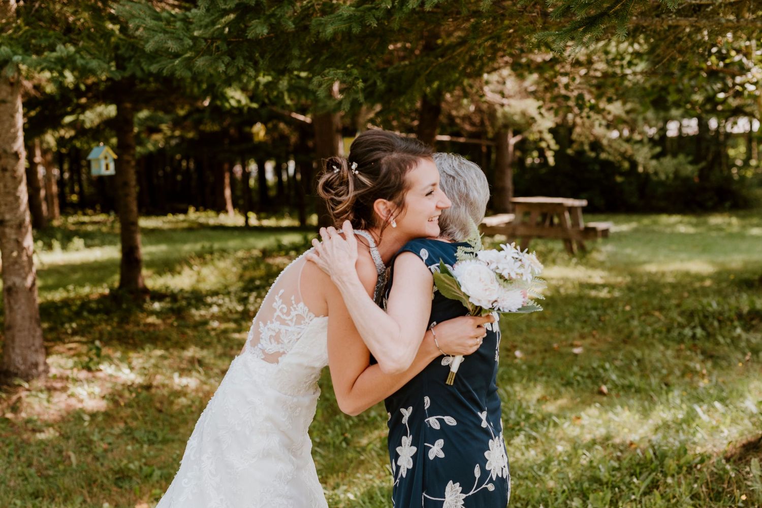 Sweet embrace between two wedding guests in a sunny outdoor garden setting.
