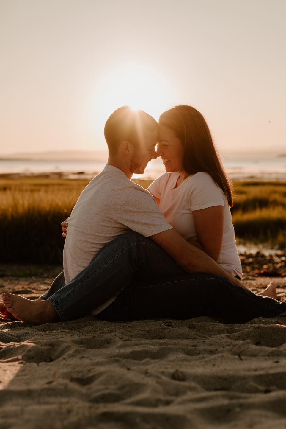 Romantic couple sitting on beach at sunset sharing tender moment together.