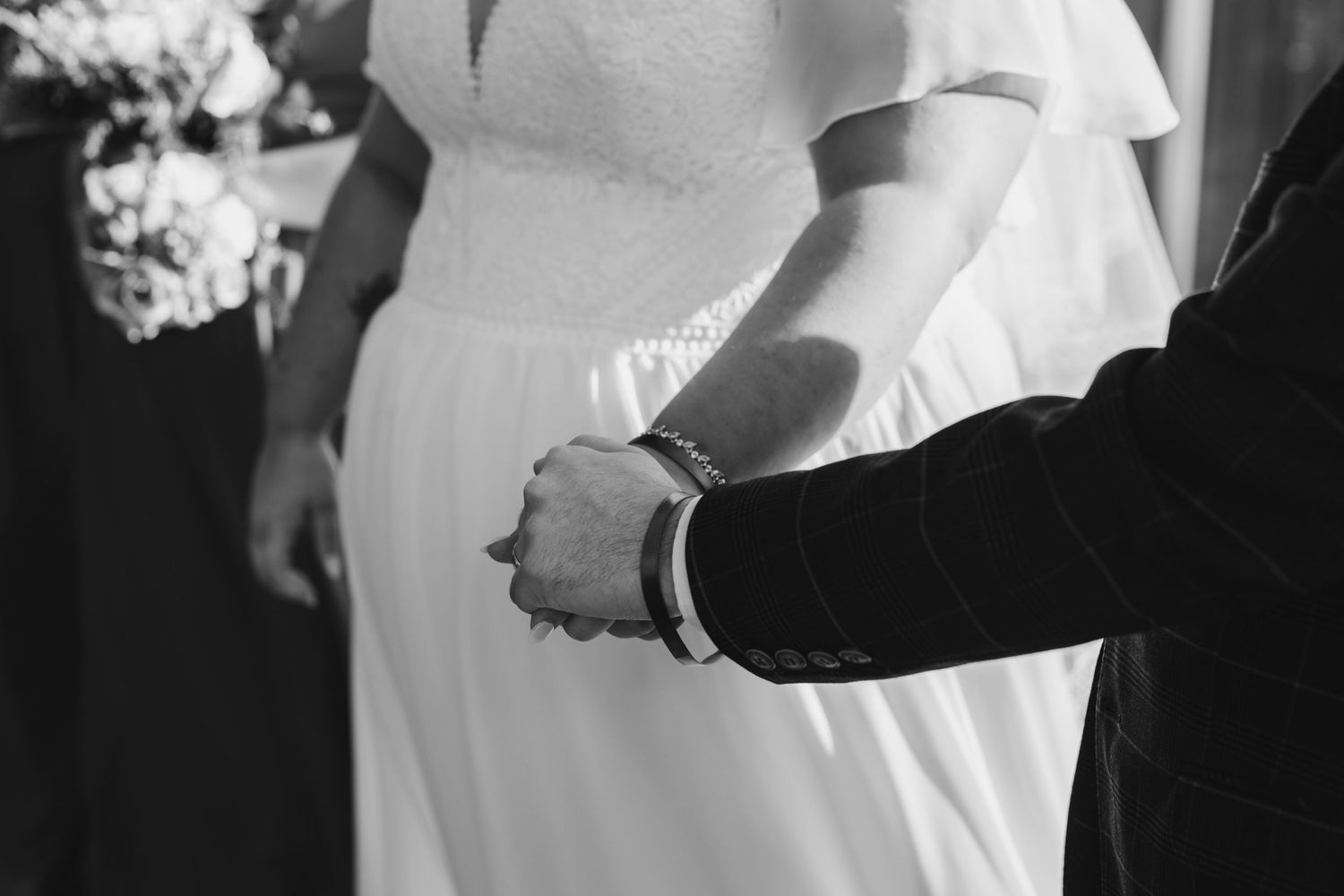 Close-up of hands during wedding ceremony with white dress in background.