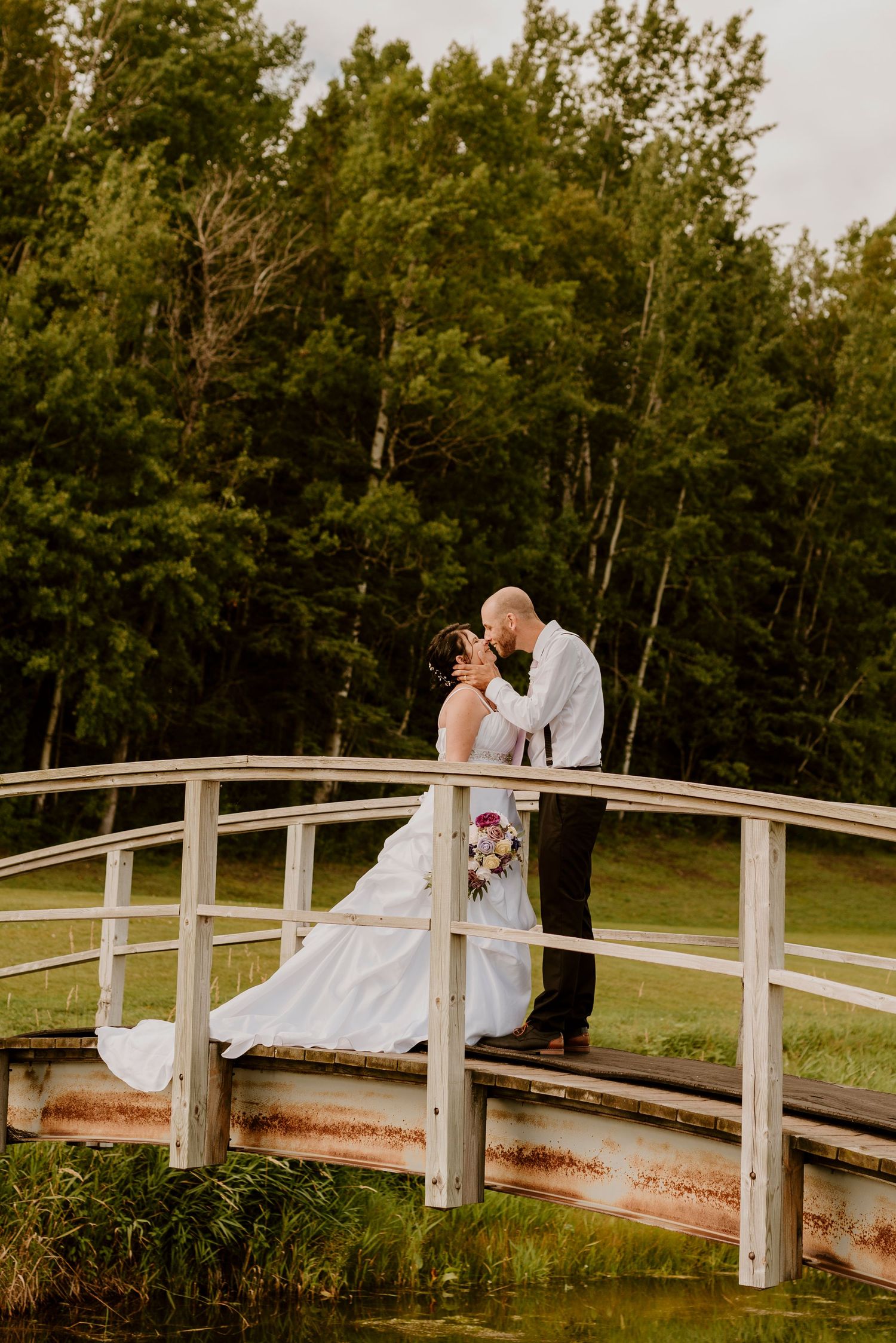 Sur un charmant pont en bois, un couple de mariés partage un moment romantique au coucher du soleil.
